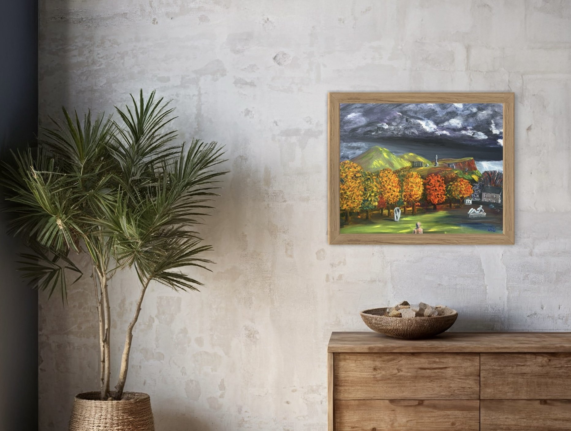 Interior of a room with a potted palm plant on the left, a wooden sideboard on the right, a woven bowl with stones on top, and a colorful landscape painting on the wall depicting trees, mountains, and cloudy sky.