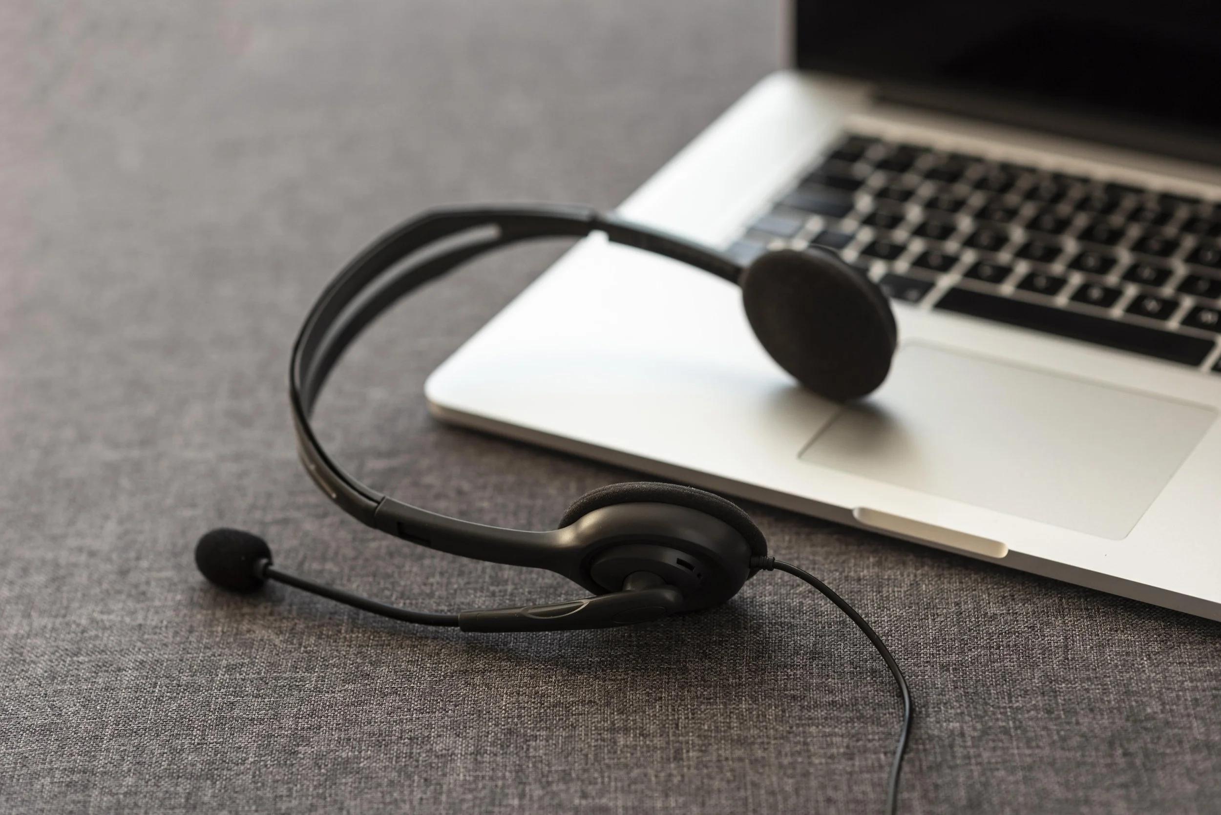 A black headset with a microphone resting on a silver laptop on a gray surface.