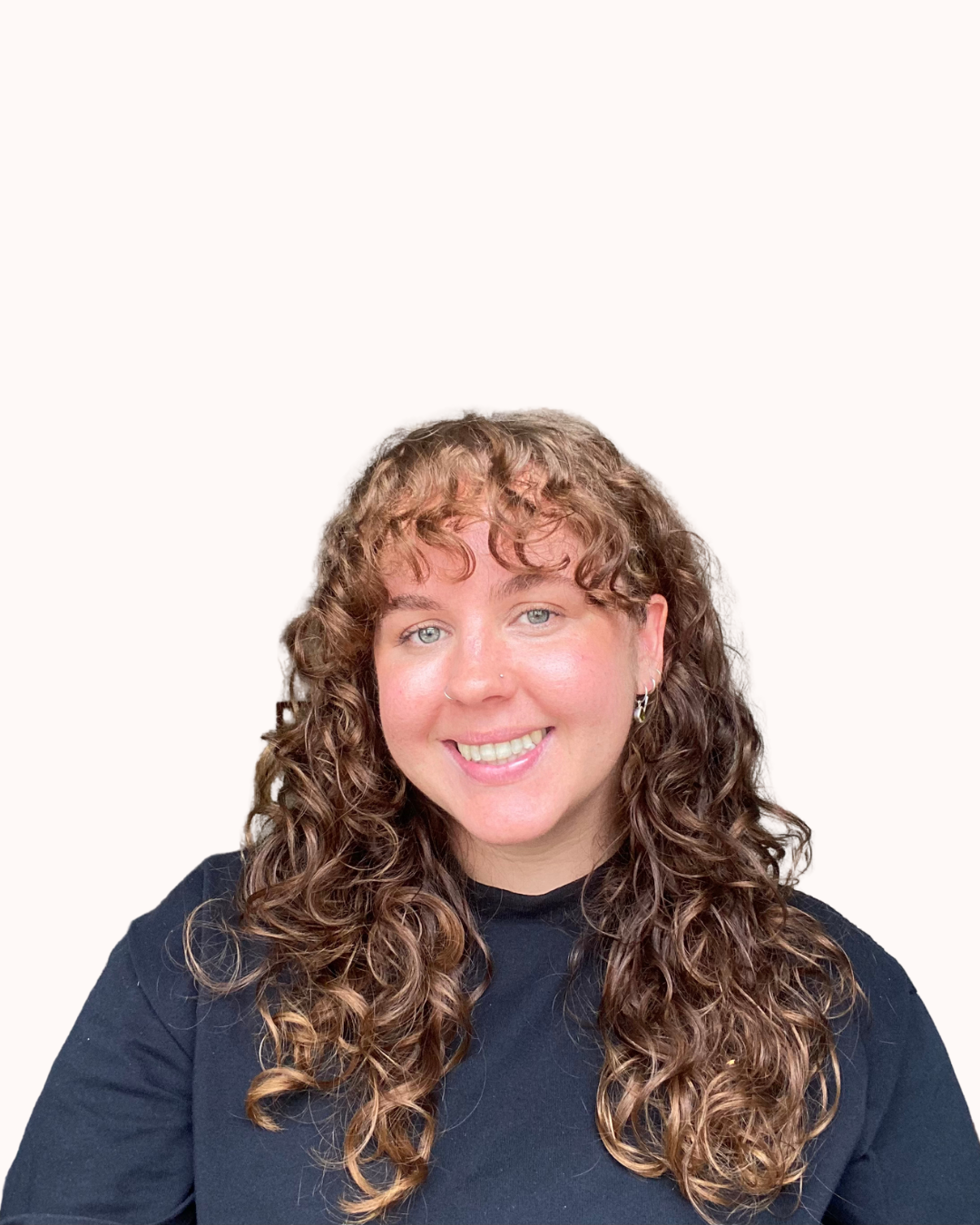A woman with curly brown hair, blue eyes, and earrings, smiling and wearing a black top against a plain white background.
