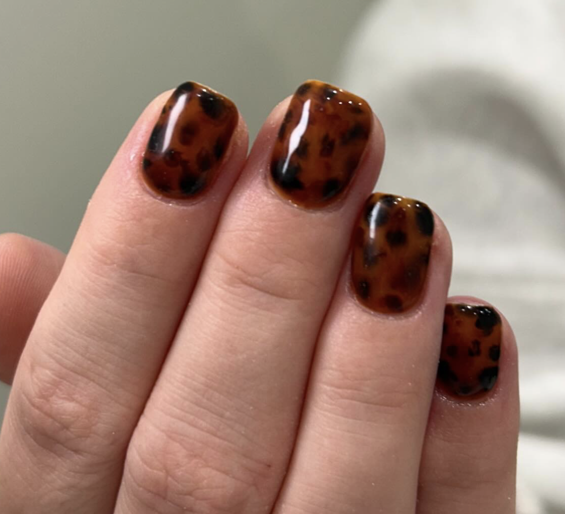Close-up of a hand with painted nails in a tortoise shell pattern of brown, black, and amber colors.