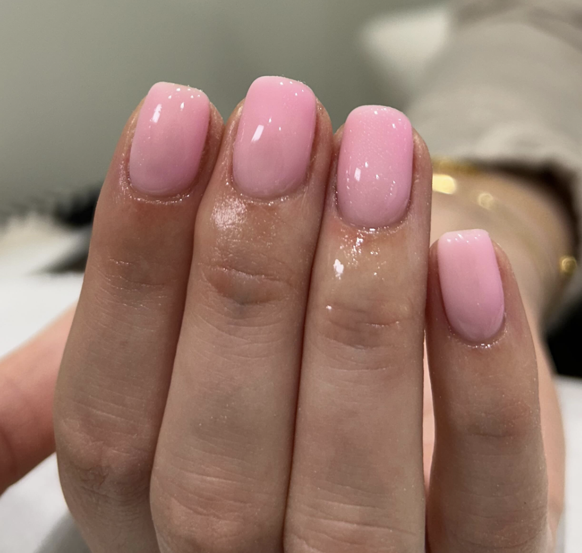Close-up of a hand with neatly manicured nails painted light pink with a glossy finish.