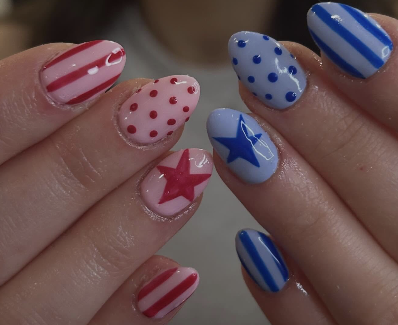 Nail art with patriotic red, white, and blue themed patterns, including stripes, polka dots, and stars.