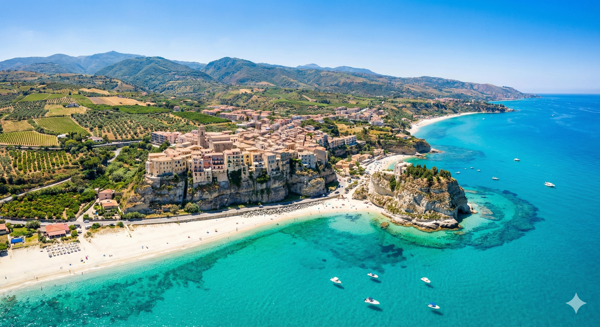 Vue aérienne d'une ville perchée sur une falaise rocheuse au bord de la mer turquoise, avec une plage de sable blanc et plusieurs navires en mer, entourée de collines verdoyantes et de montagnes en arrière-plan, sous un ciel bleu clair.