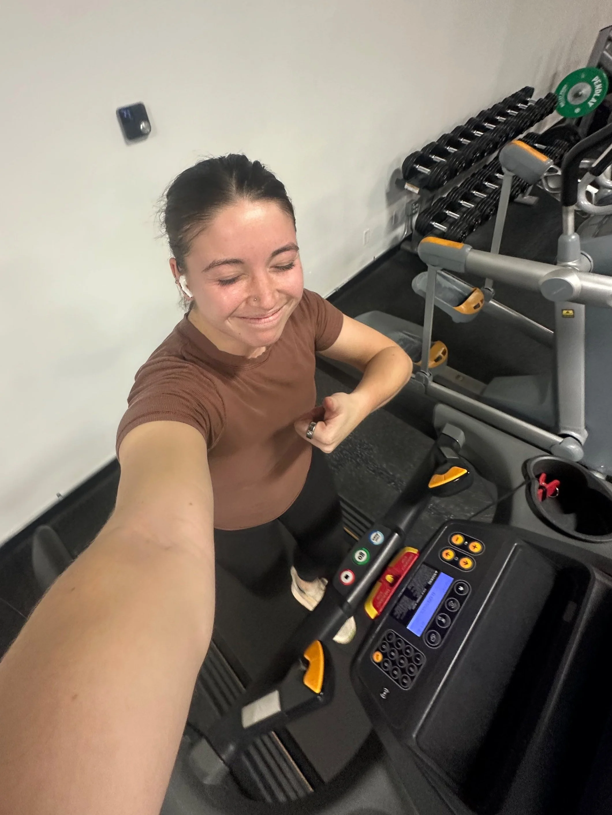 Person taking a selfie on a treadmill in a gym, with weights in the background.