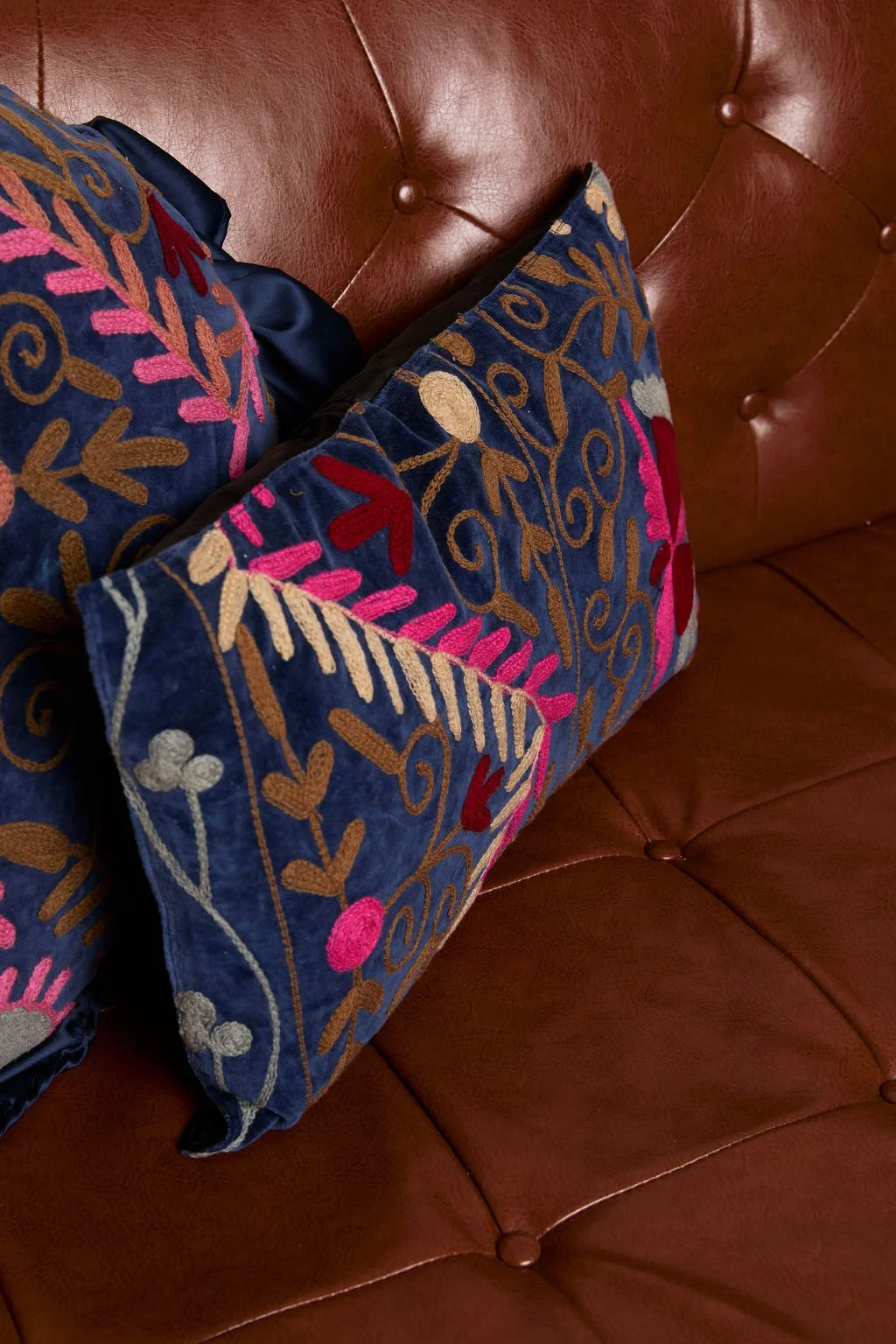 Colorful embroidered pillows on a brown leather tufted sofa.
