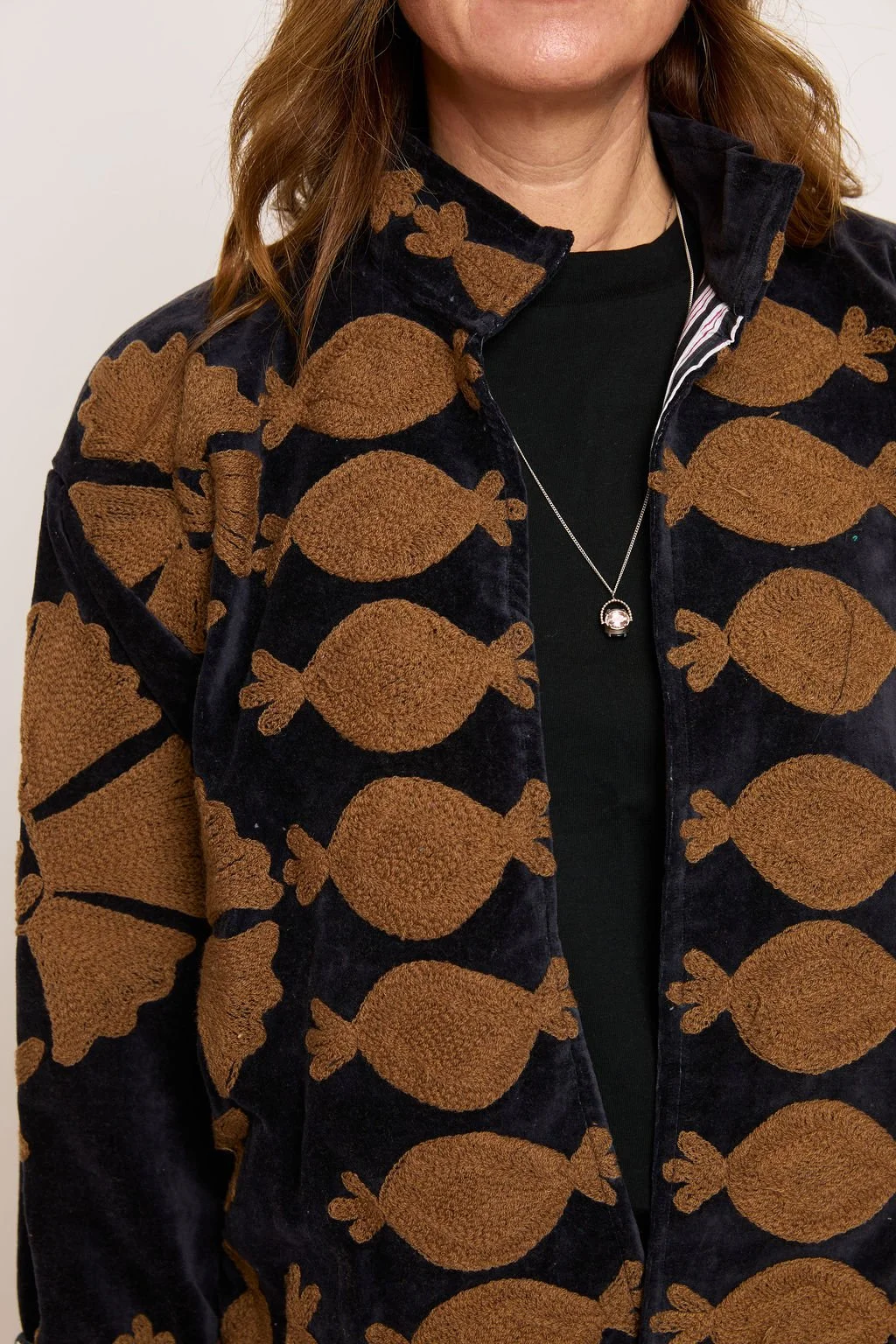A woman wearing a black velvet jacket with large orange candies printed on it, a black shirt underneath, and a silver necklace.