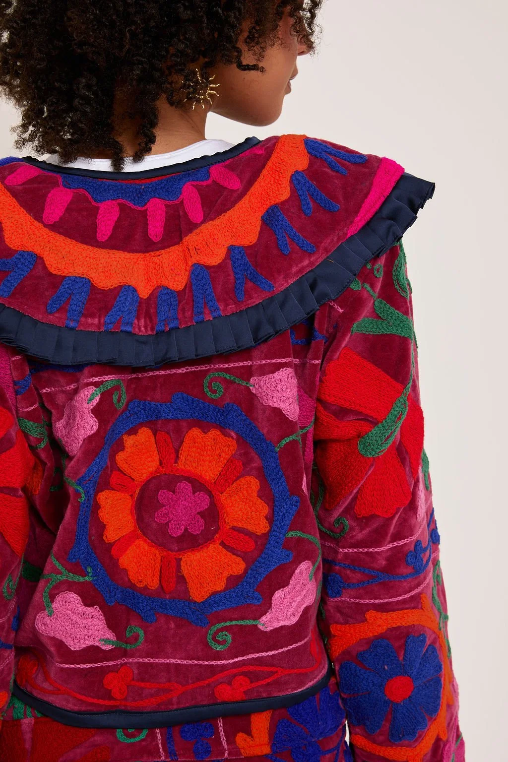Close-up of a woman wearing a colorful embroidered jacket with floral and abstract patterns, and a large decorative collar with ruffled edges.