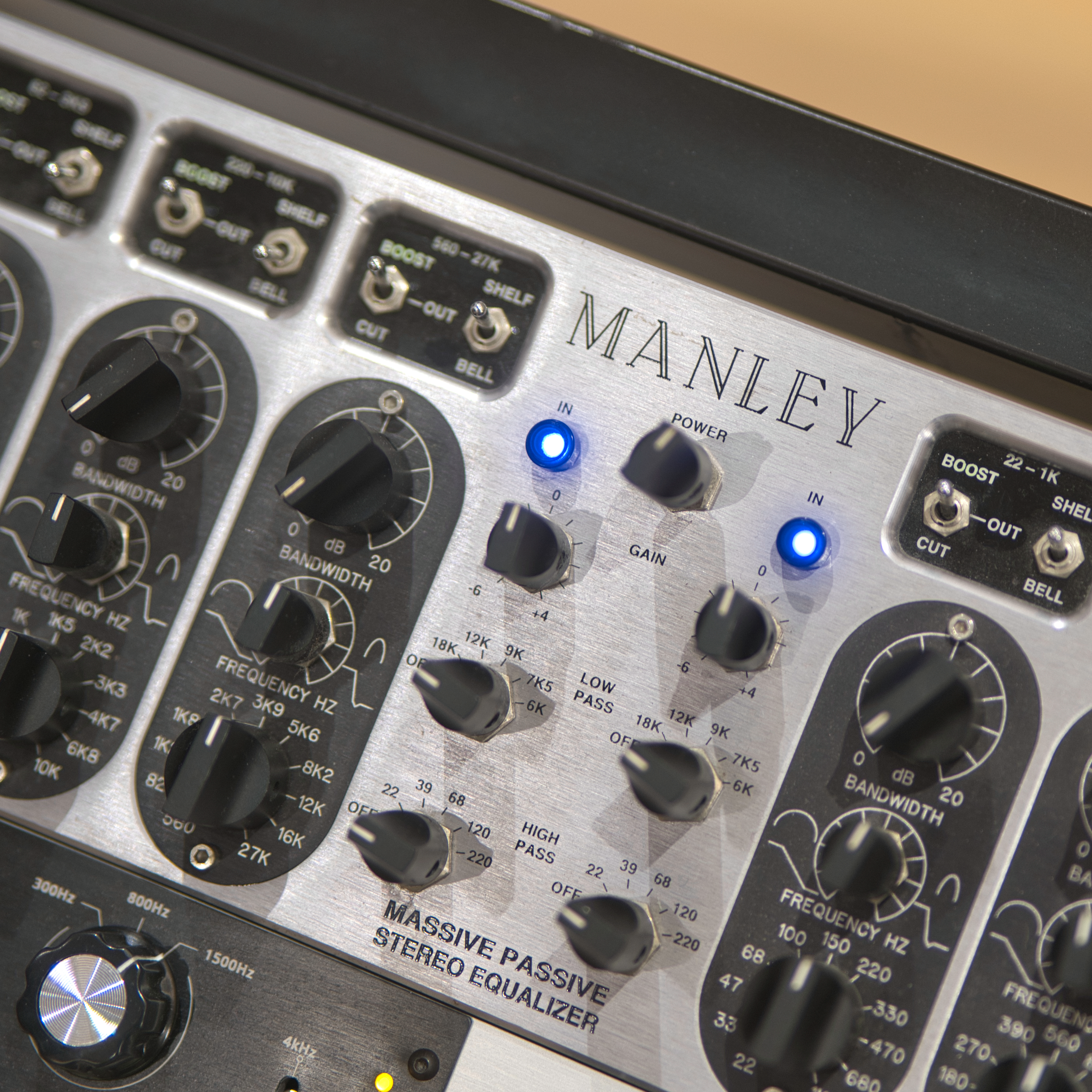 Close-up of a Manley stereo equalizer with various knobs and switches, illuminated blue LED indicators, and brand name visible on a silver metal panel.