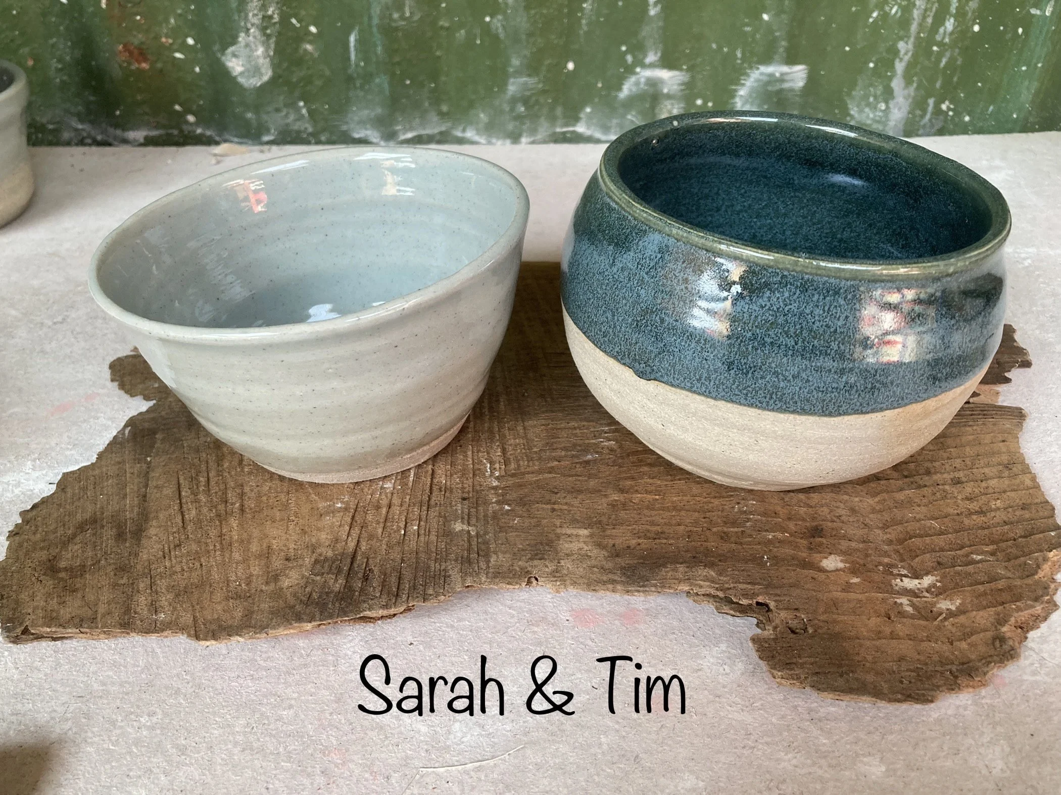 Two handmade ceramic bowls resting on a piece of wood with the text 'Sarah & Tim' beneath them.