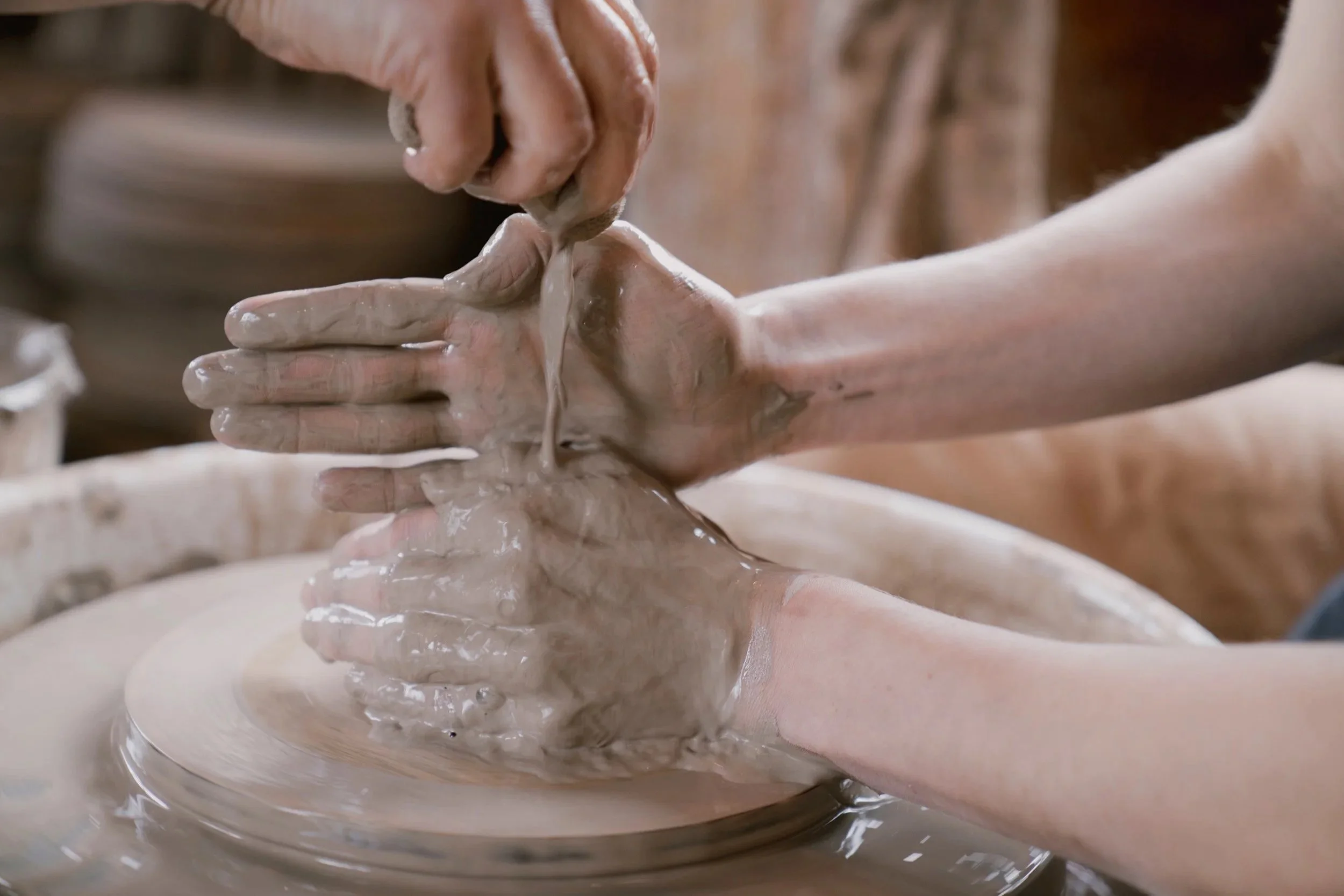 Person shaping wet clay on a pottery wheel with their hands.