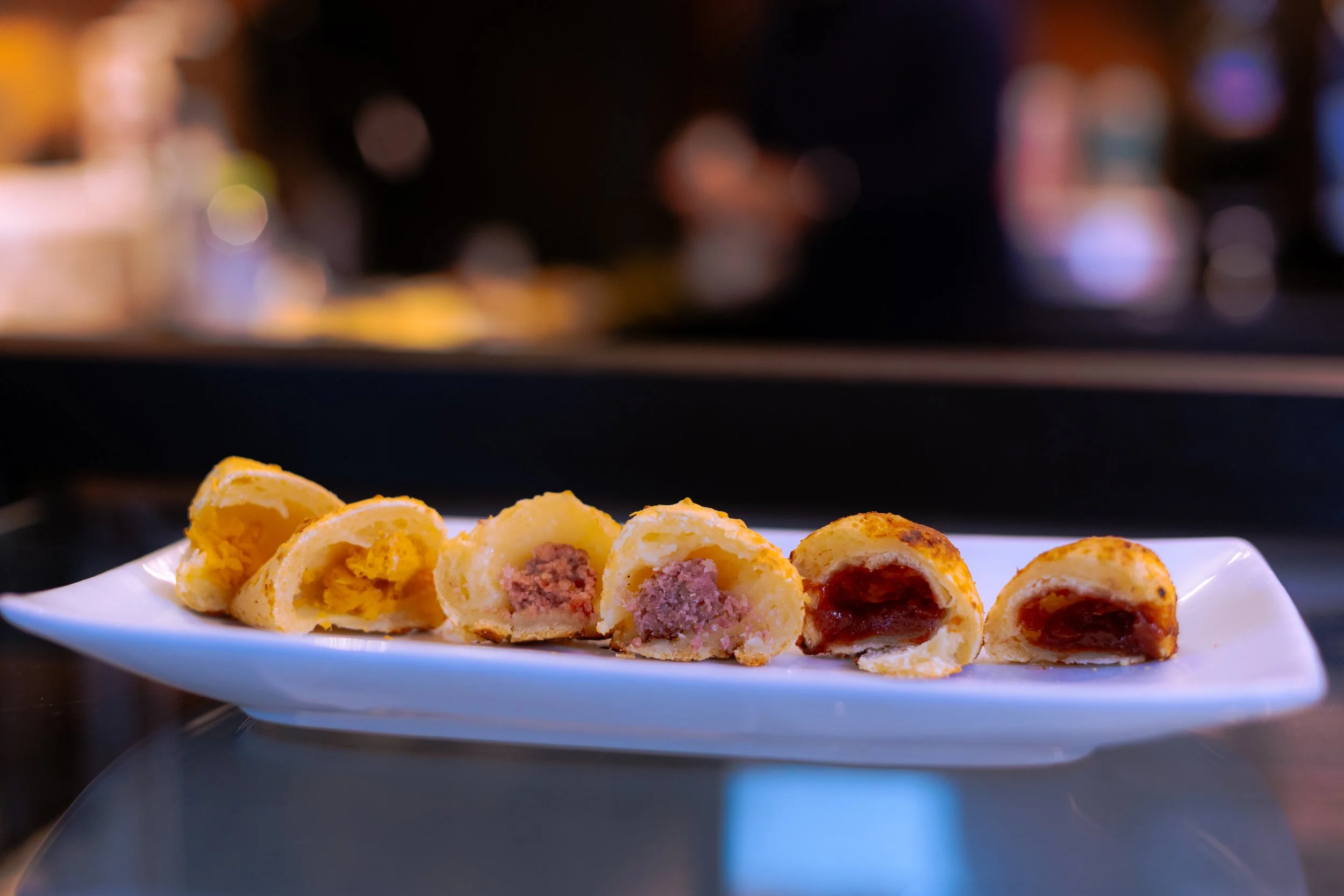 Prato com mini pães de queijo recheados de diversos sabores em uma superfície brilhante.