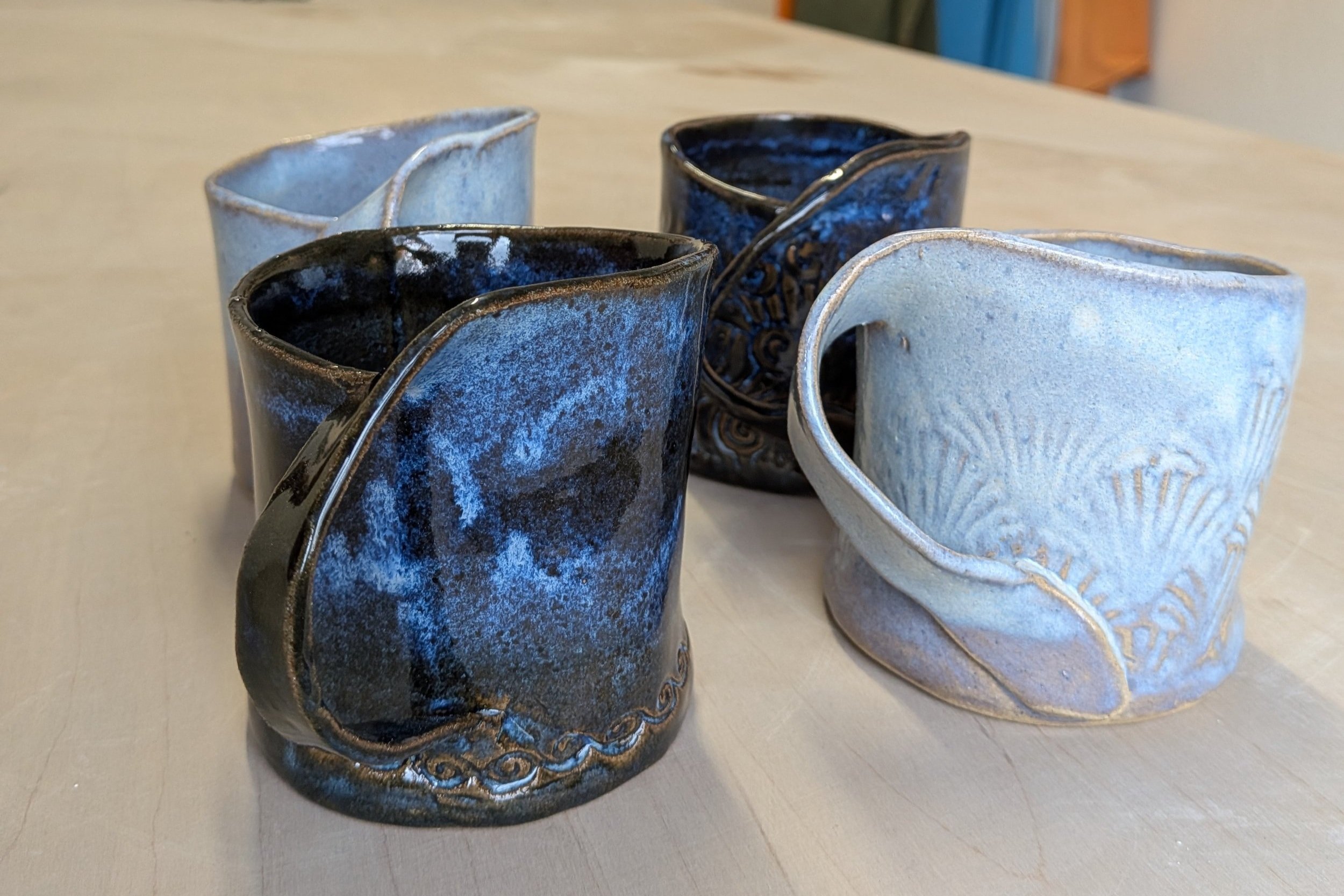 Handcrafted ceramic mugs with unique blue glaze and textured designs on a wooden surface.