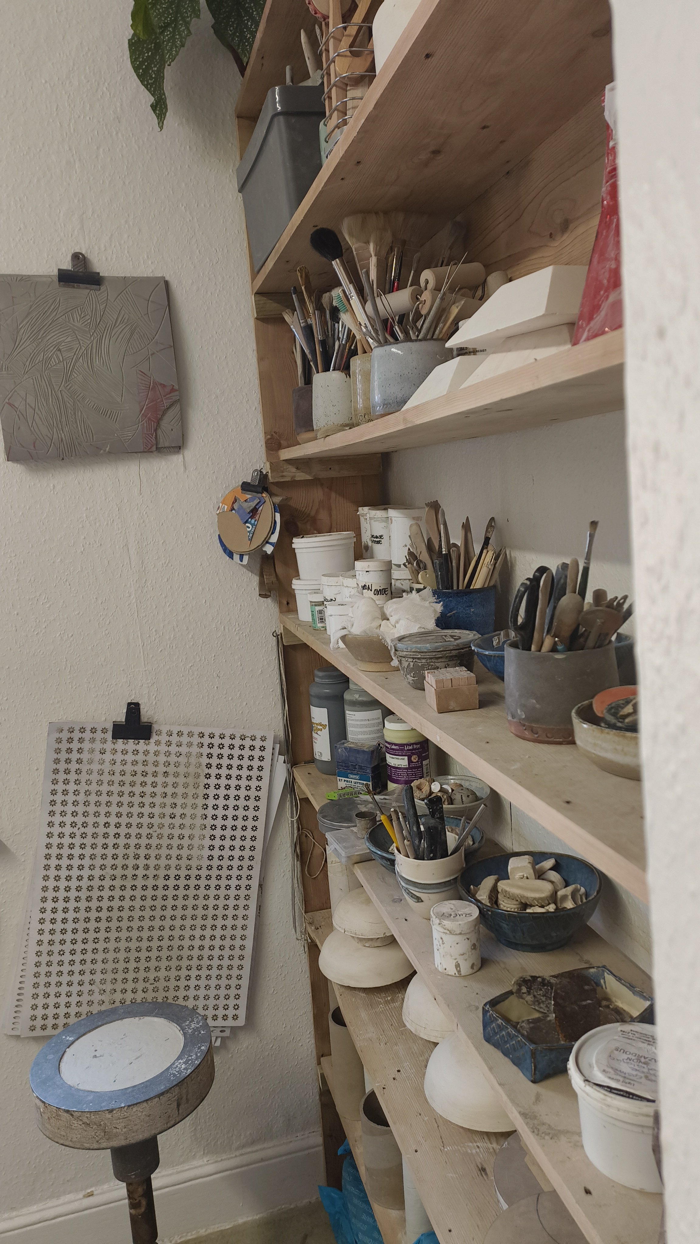 Pottery workspace with tools, brushes, paints on shelves.
