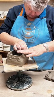 Person shaping clay on a pottery wheel at a studio