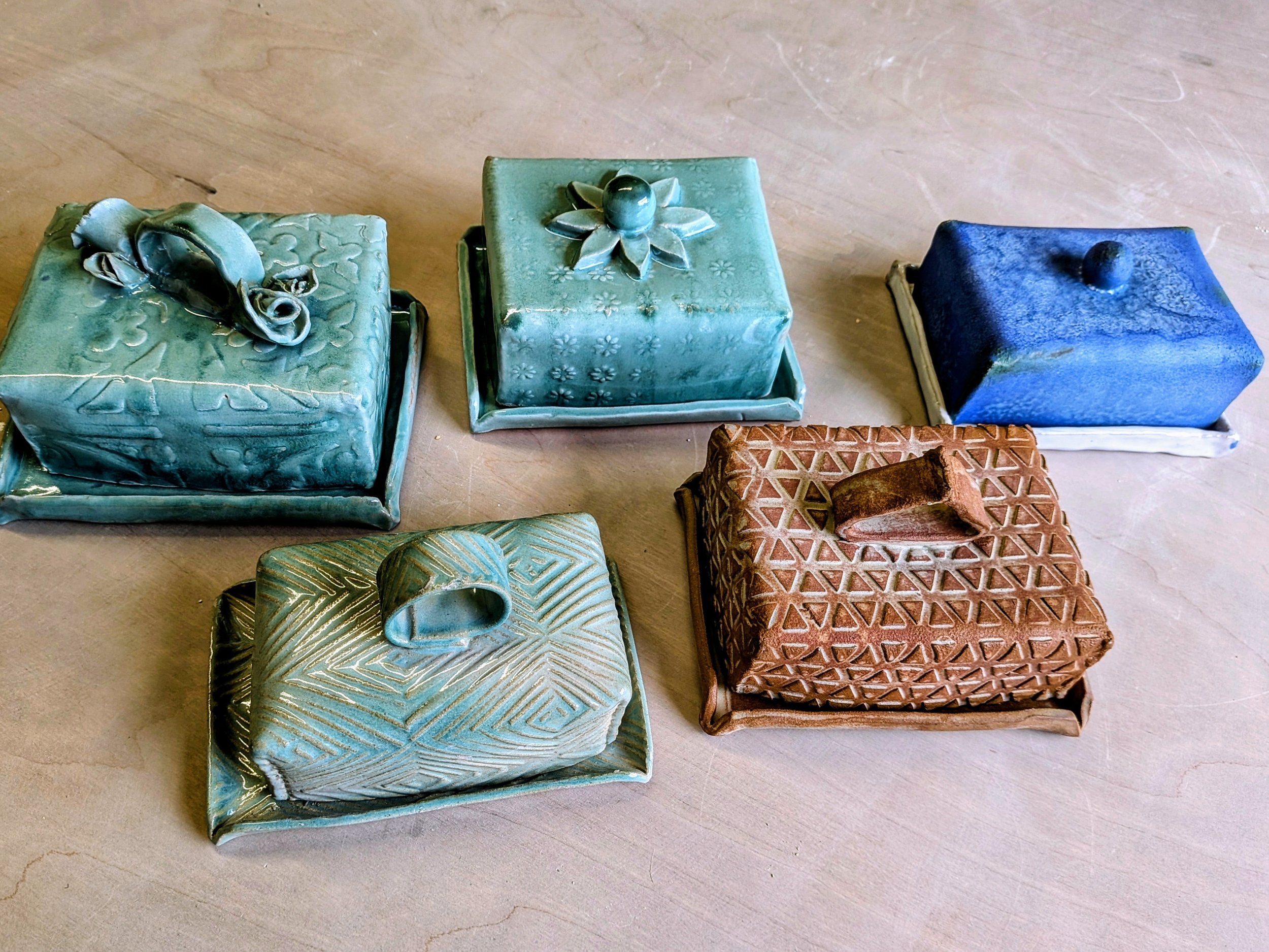 Handcrafted ceramic butter dishes with various designs and colors on a wooden surface.