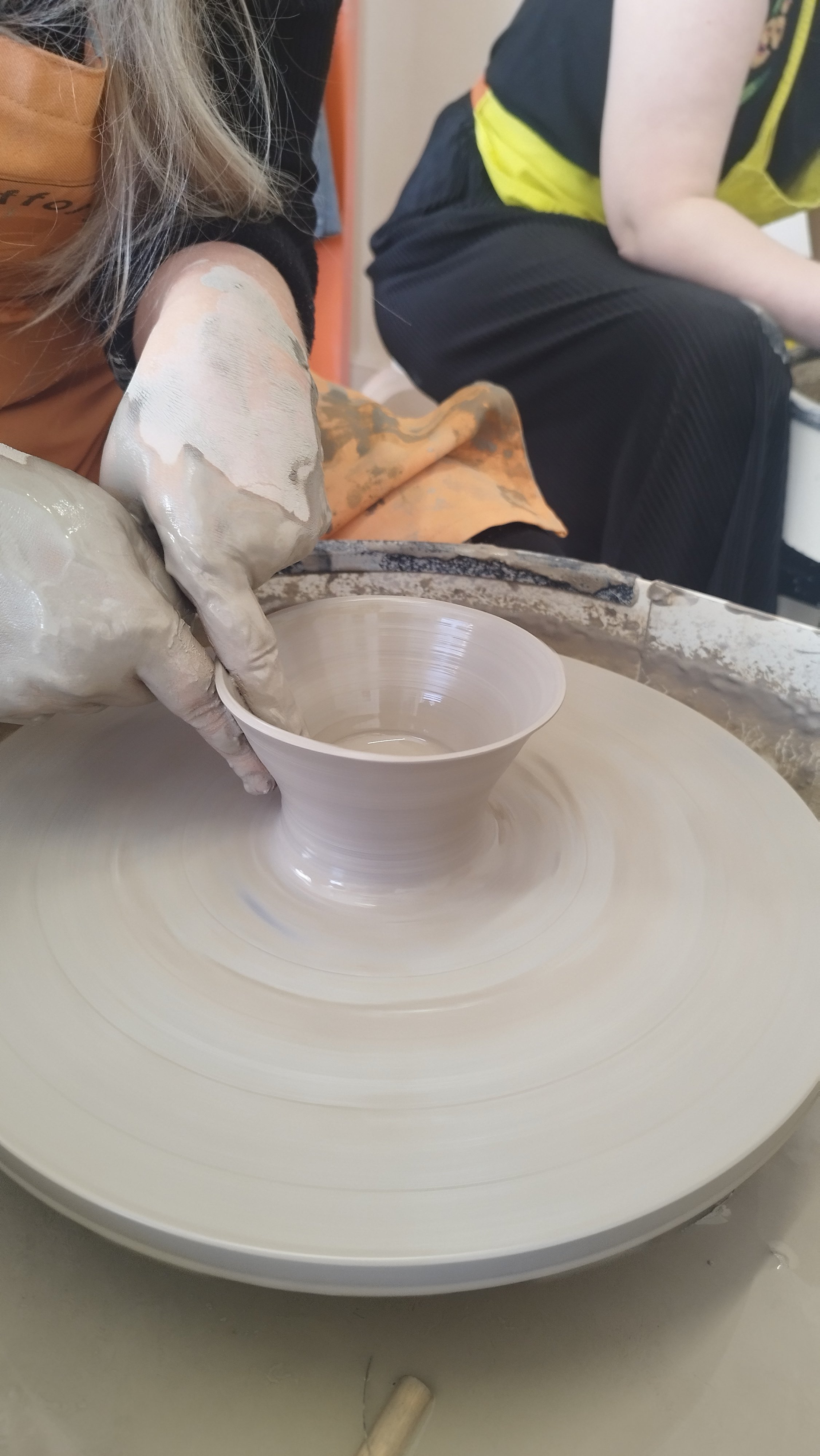 Person shaping clay on a pottery wheel, hands covered in clay, creating a ceramic bowl.
