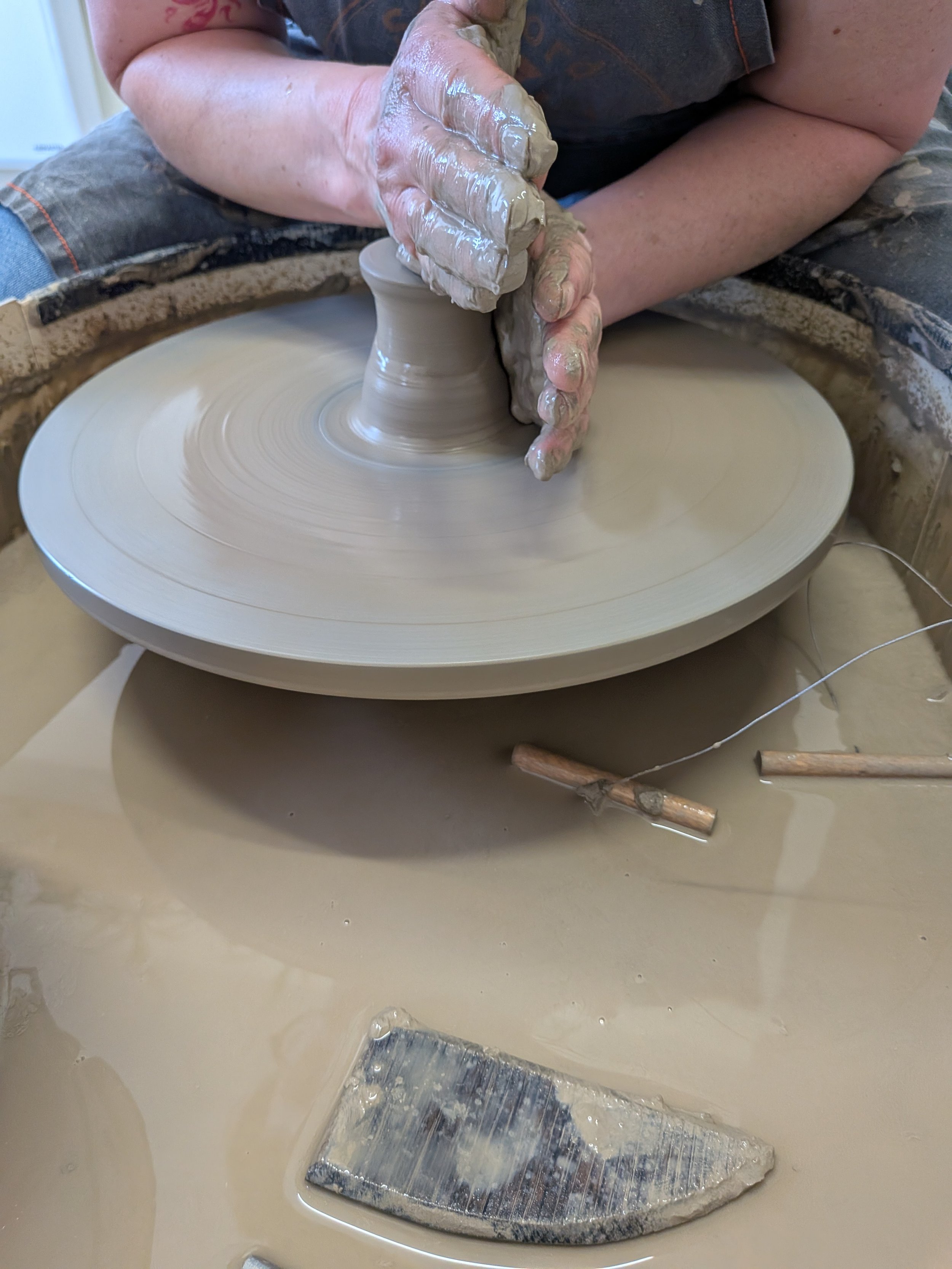 A person working with clay on a pottery wheel, shaping it with their hands.