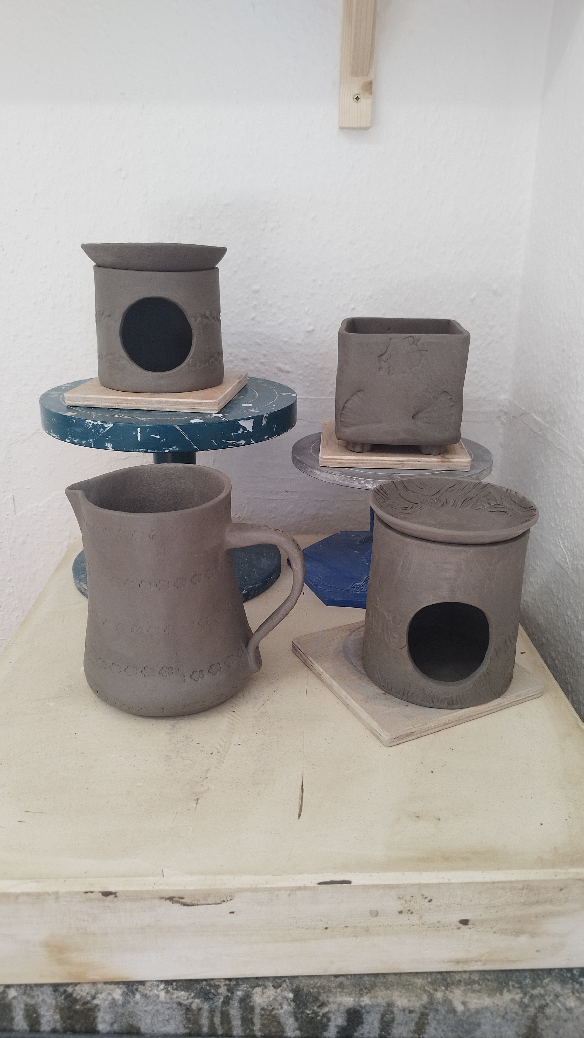 Clay pottery pieces in various shapes, including a pitcher and cylindrical candle holders, on a wooden surface.