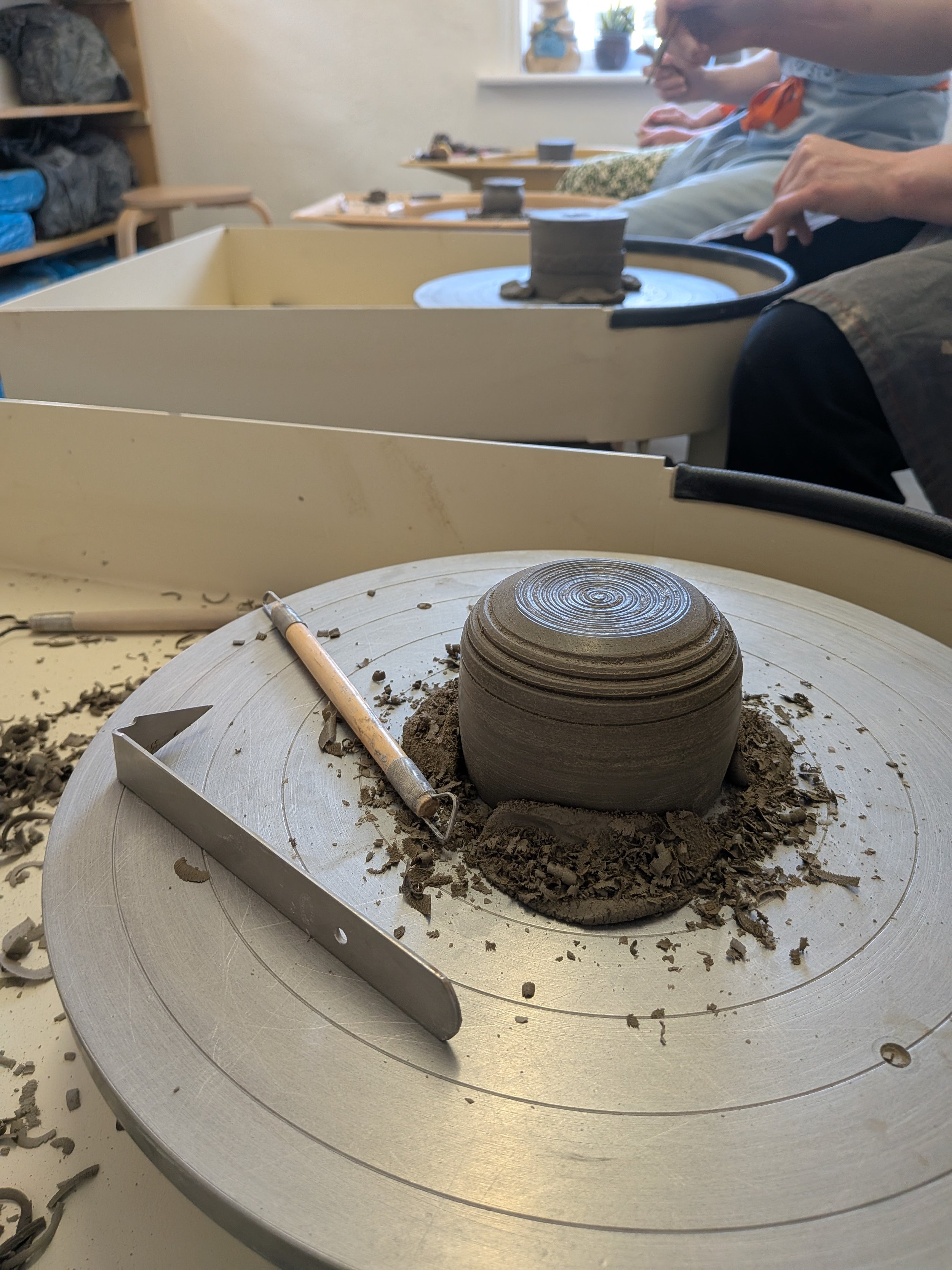 Pottery wheel with clay piece and tools in a ceramics studio.