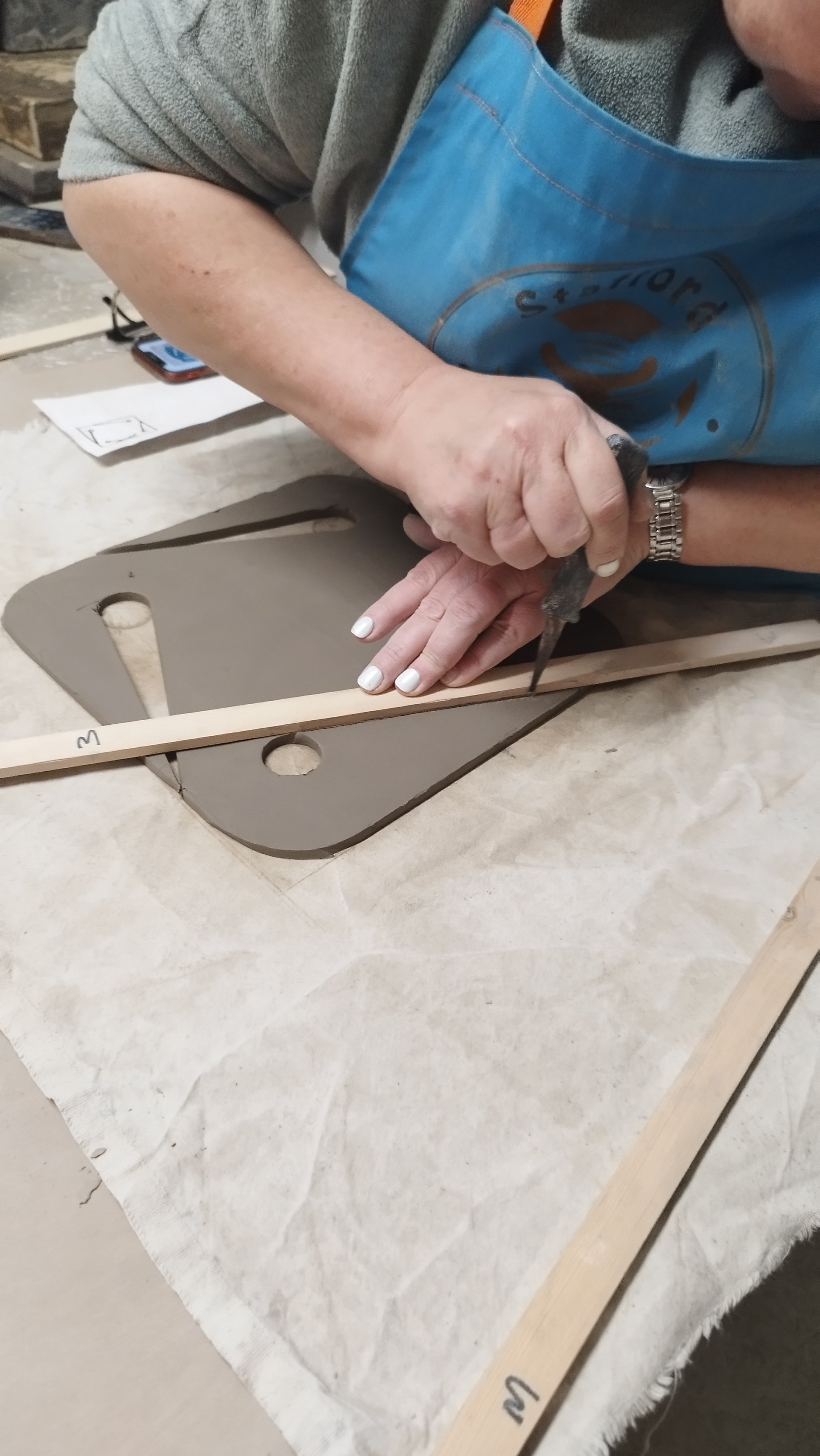 Person shaping clay using a wooden tool on a table.