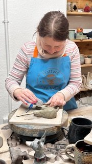 Person sculpting clay in pottery studio wearing blue apron