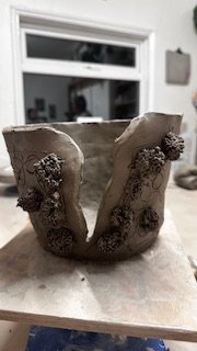 Handmade ceramic pot with textured surface, partially split, on a wooden table in a studio setting.