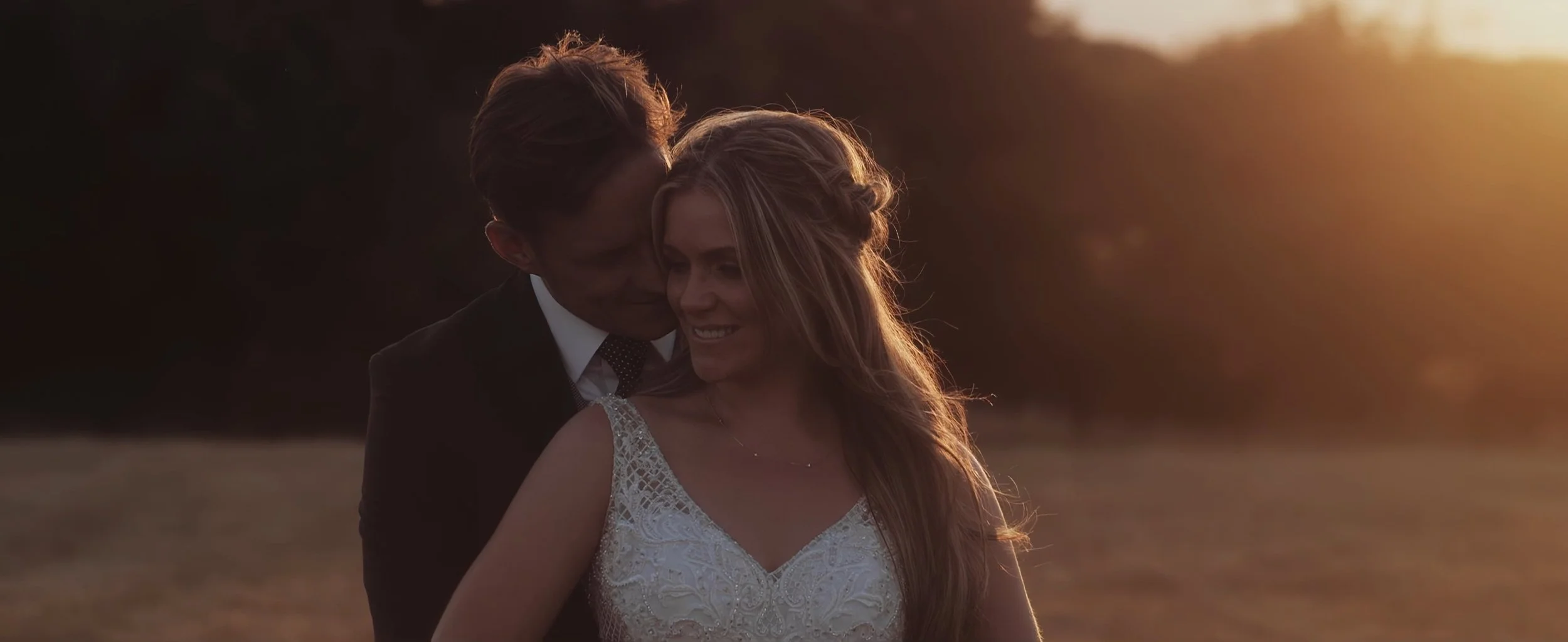 Ashley and Chris embracing at sunset in golden field