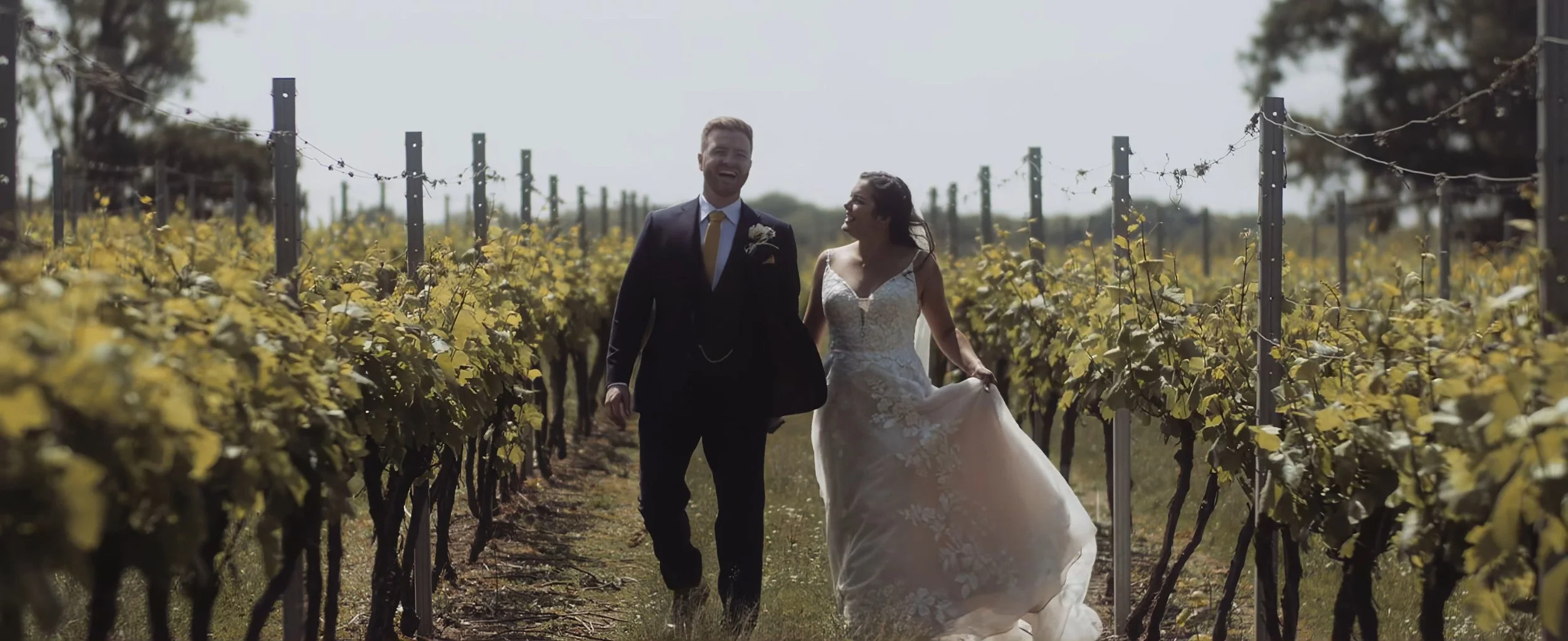 Alethea and Neil walking hand in hand through vineyard