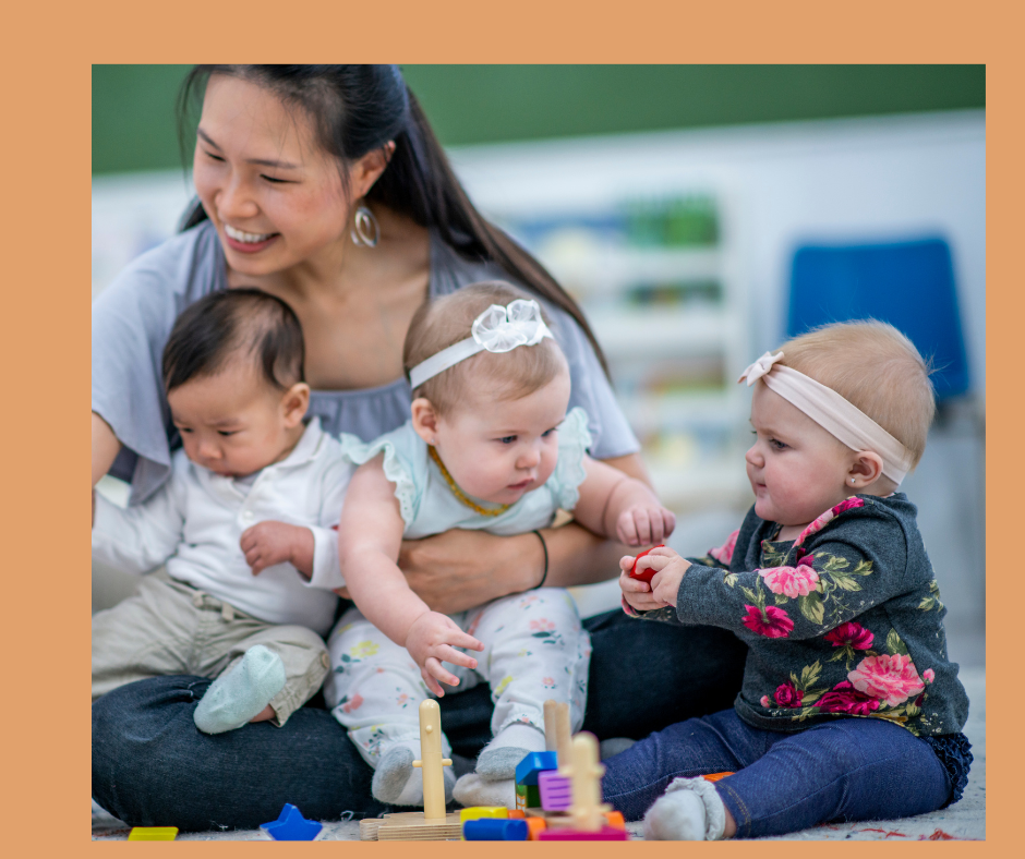 Woman holding two babies while another baby plays with a toy.