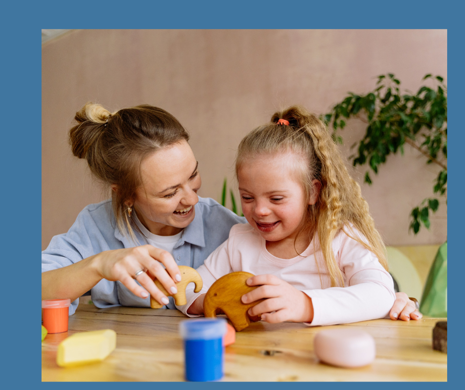 A woman and a child playing with clay and wooden toys at a table, smiling and interacting. Indoor setting with plants in the background.