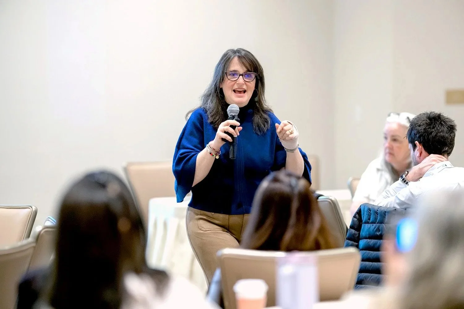 Woman speaking into a microphone at a conference or seminar, with audience members listening.
