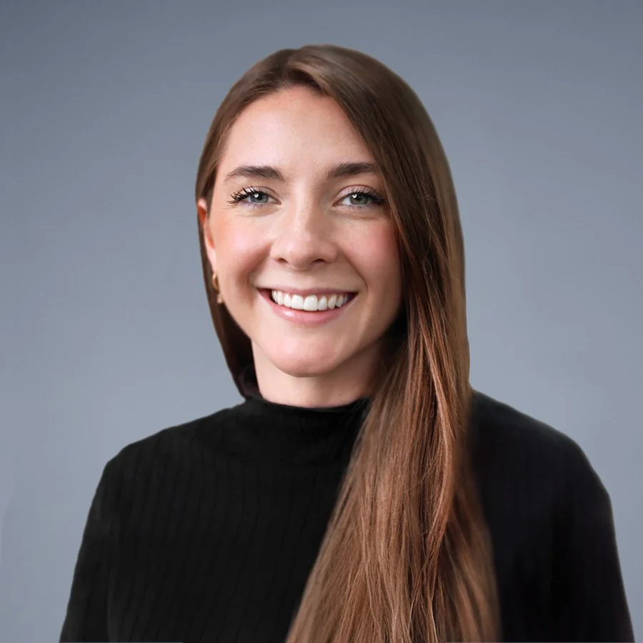 A woman with long brown hair, smiling, wearing a black turtleneck, against a gray background.