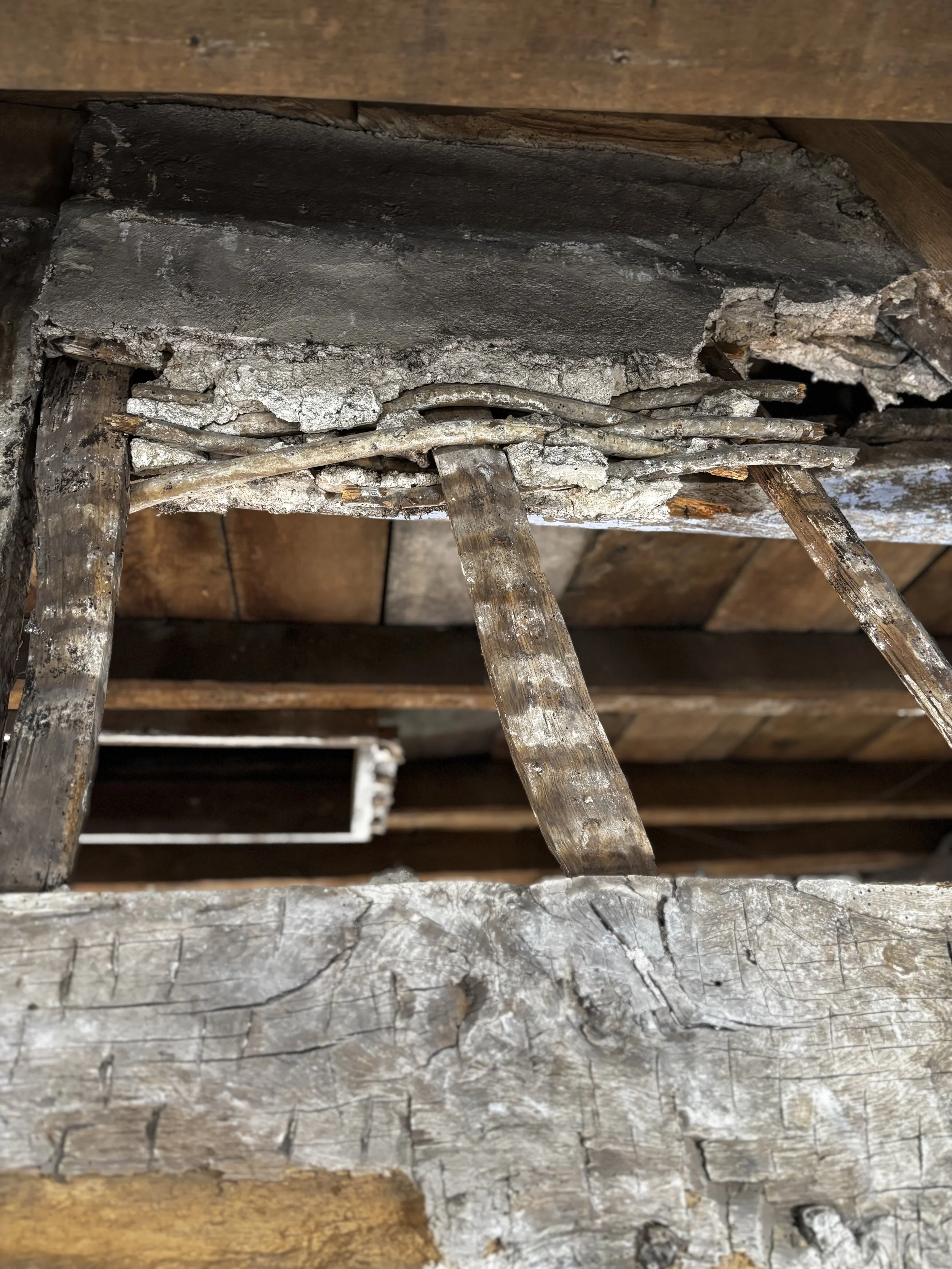 Close-up of a damaged wooden ceiling with a broken concrete block and scattered debris.