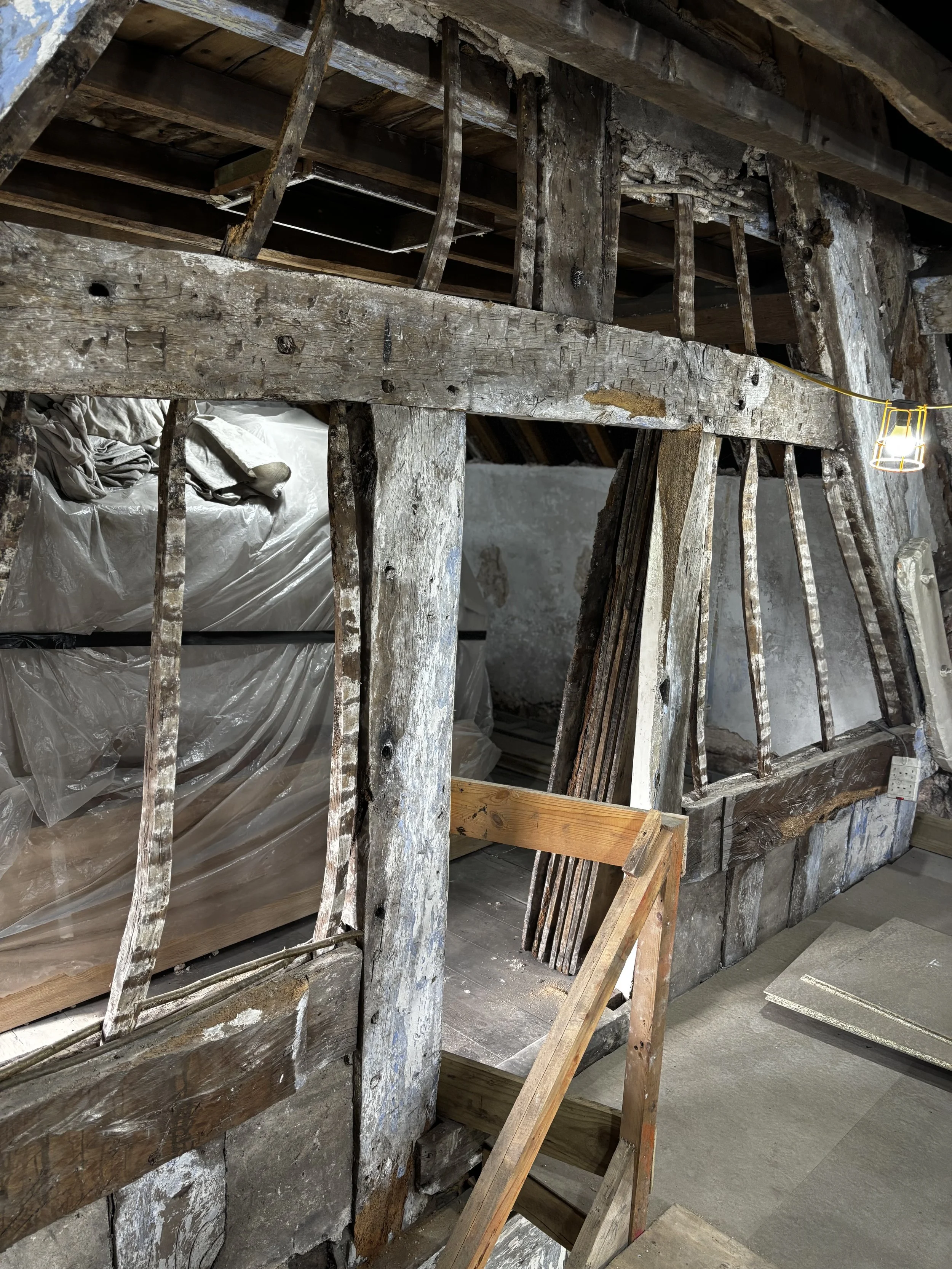 The image shows an old, weathered wooden staircase with rusted metal railings. It appears to be part of a building under renovation or disrepair, with plastic sheeting and construction materials visible behind it. A small lantern light is hanging on a wire to the right.