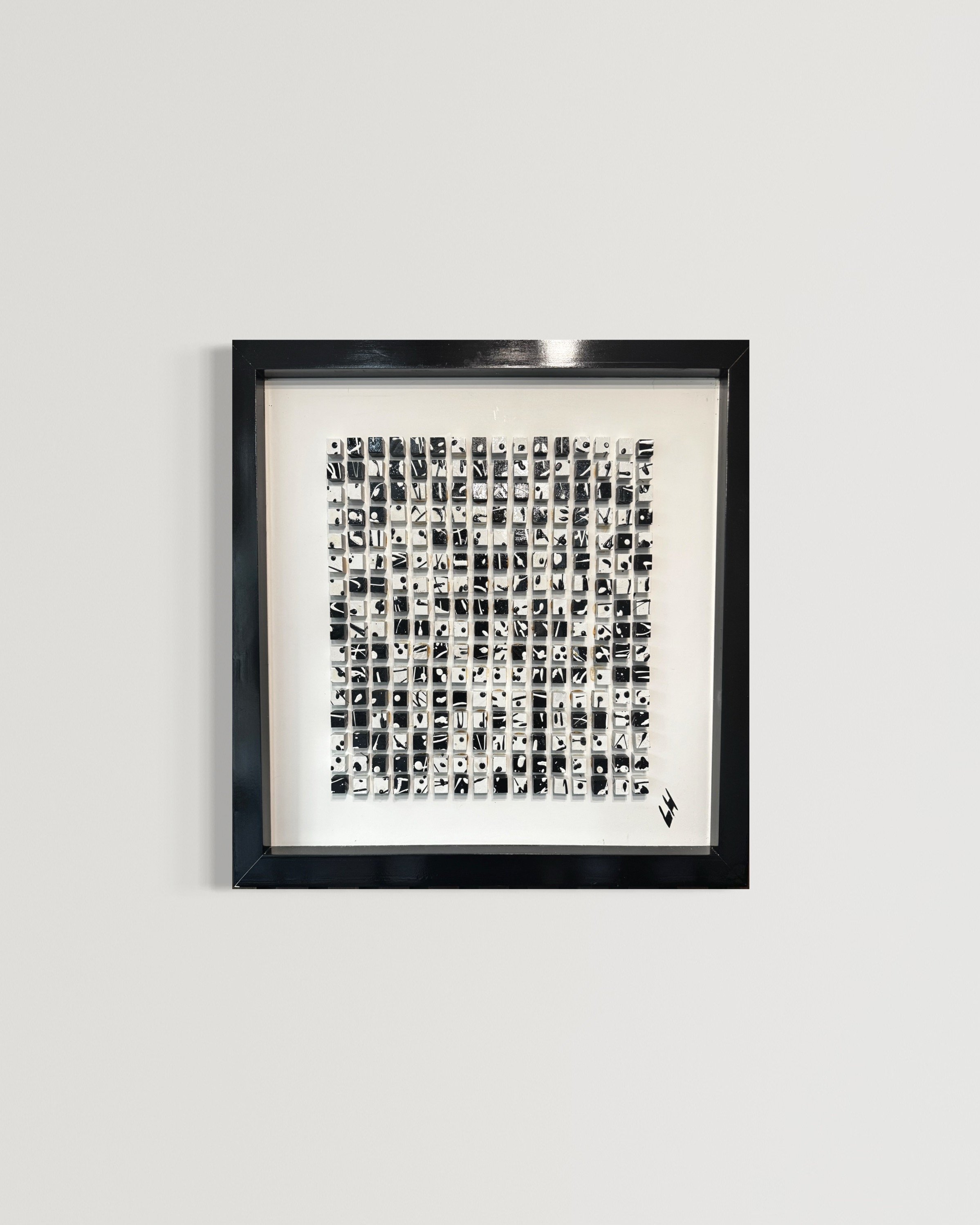 Framed black and white abstract artwork with small squares on a white background, mounted on a plain white wall