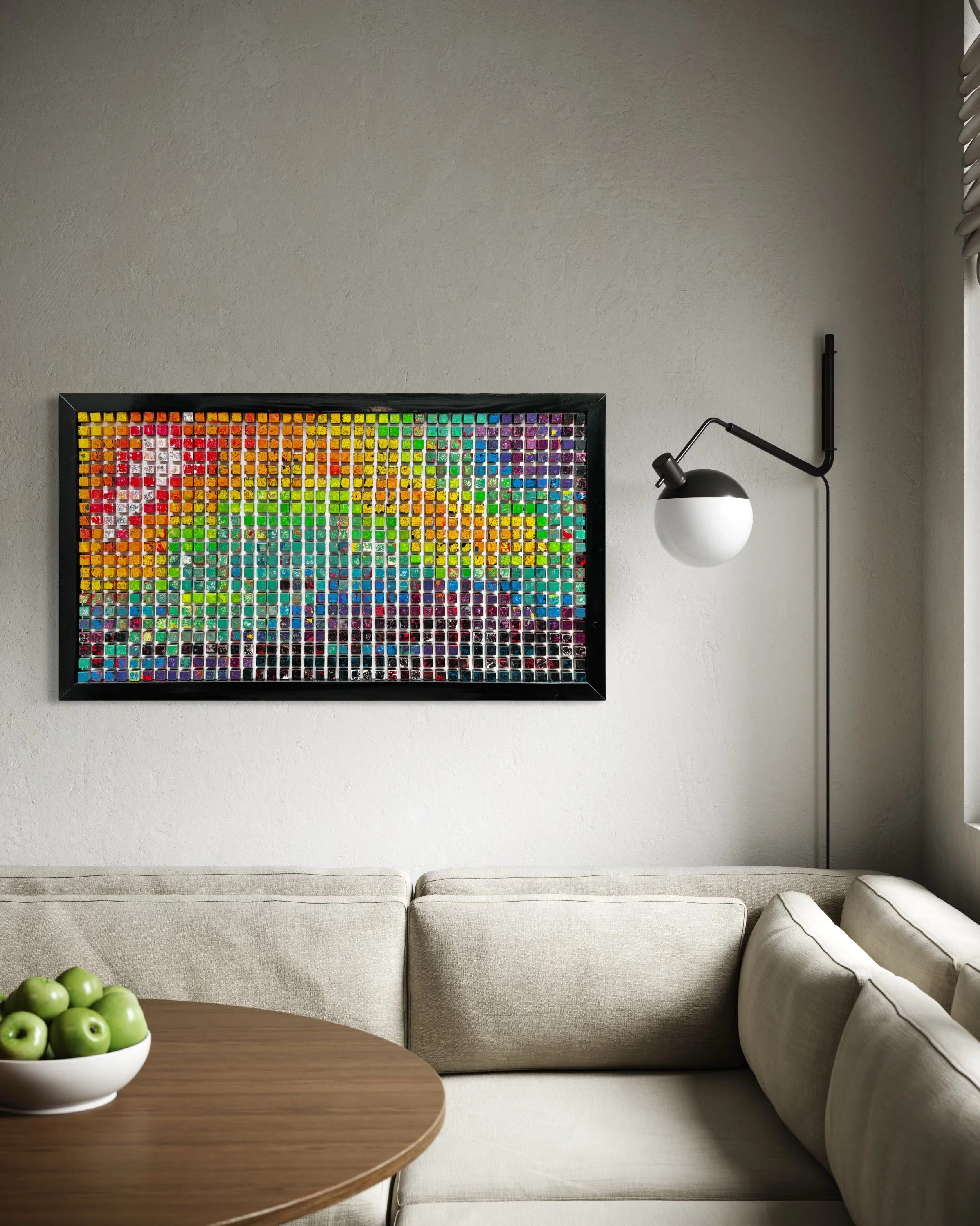 Living room with a beige sectional sofa, a wooden coffee table with green apples, a framed artwork made of small colorful tiles, and a black and white wall-mounted lamp.
