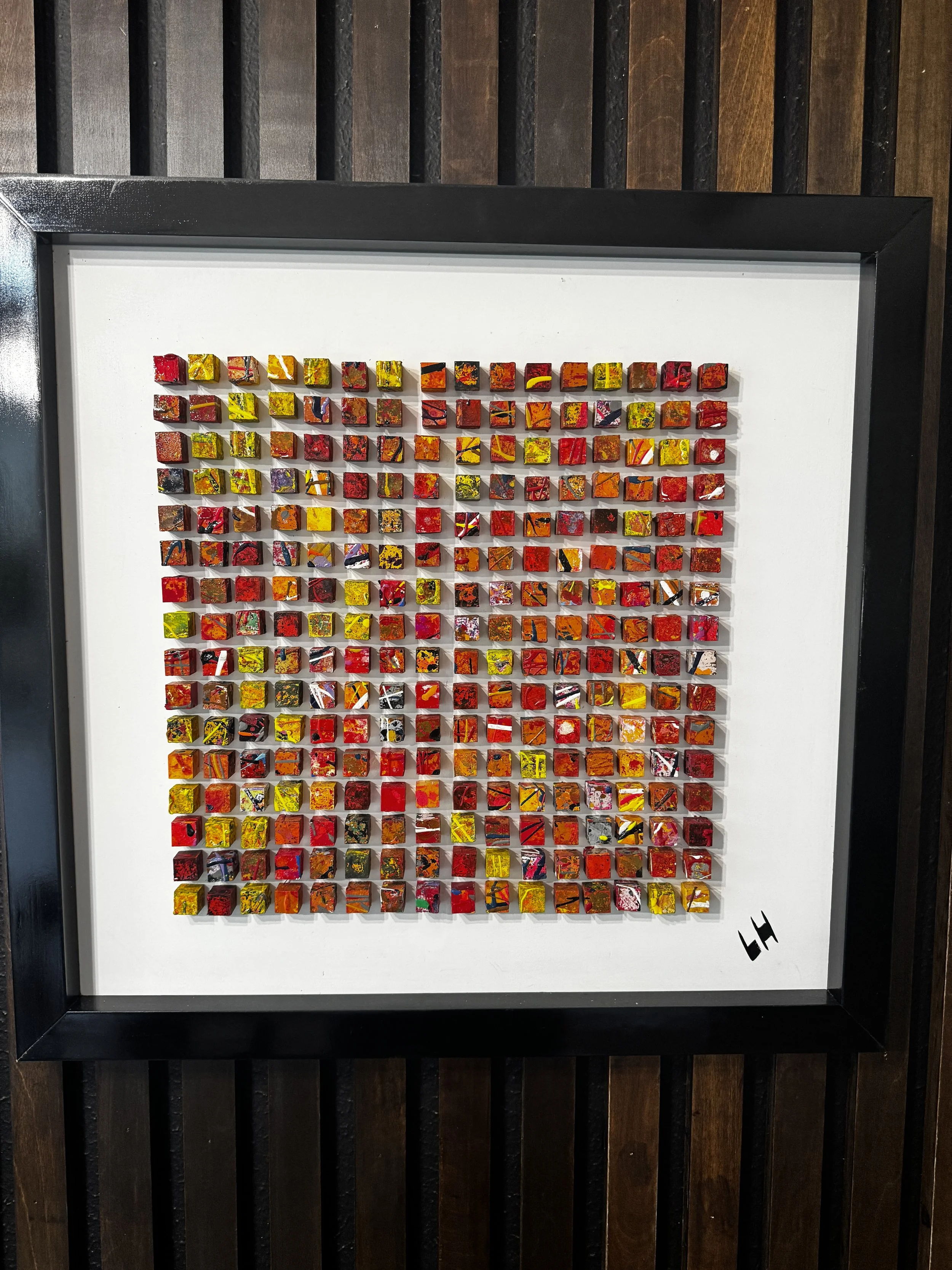 Colorful mosaic art piece with many small square tiles in red, yellow, orange, purple, black, and white, arranged on a white background, framed with a black border.