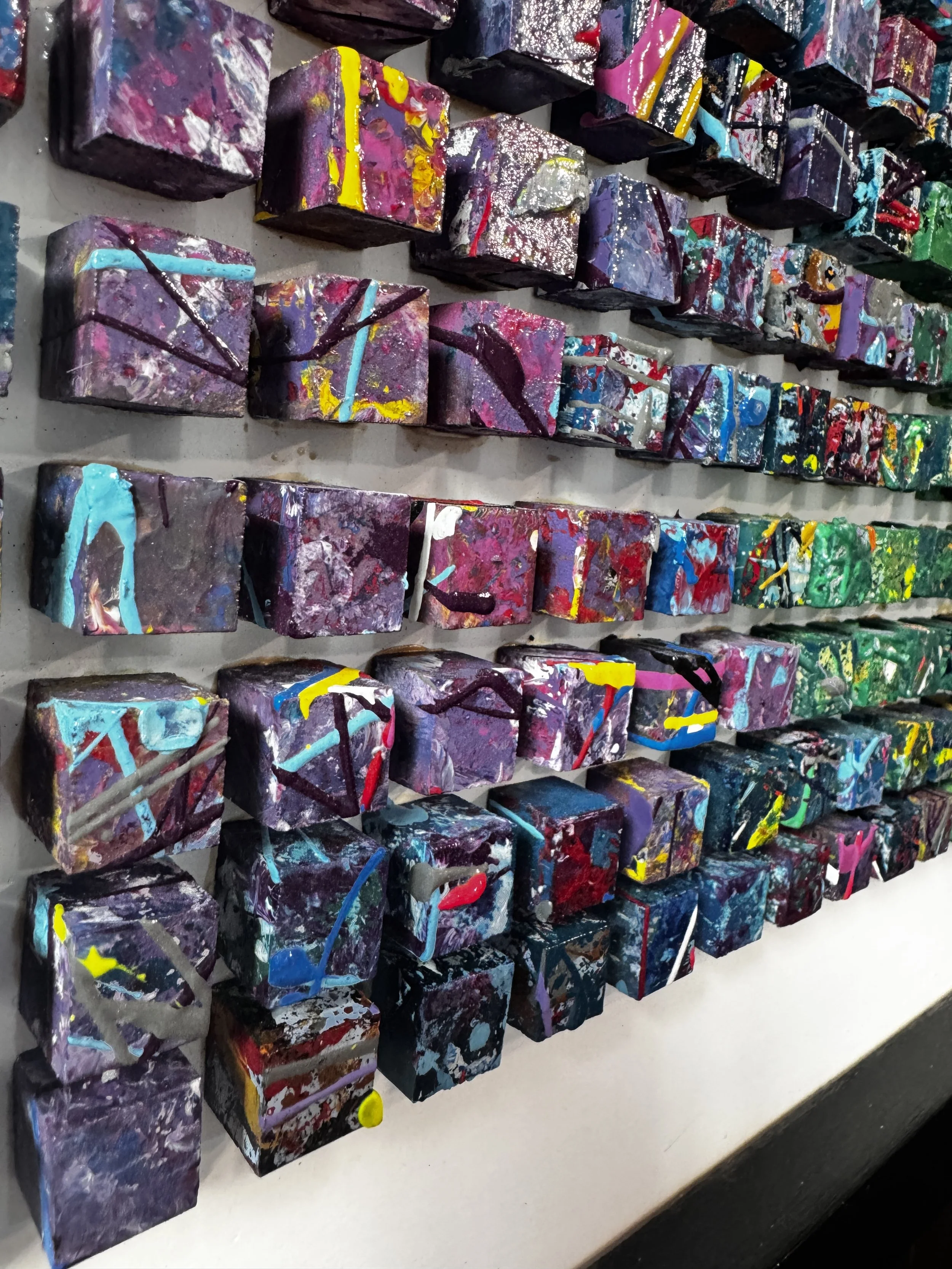 Colorful abstract artwork made of painted, textured cubes arranged in rows on a wall.