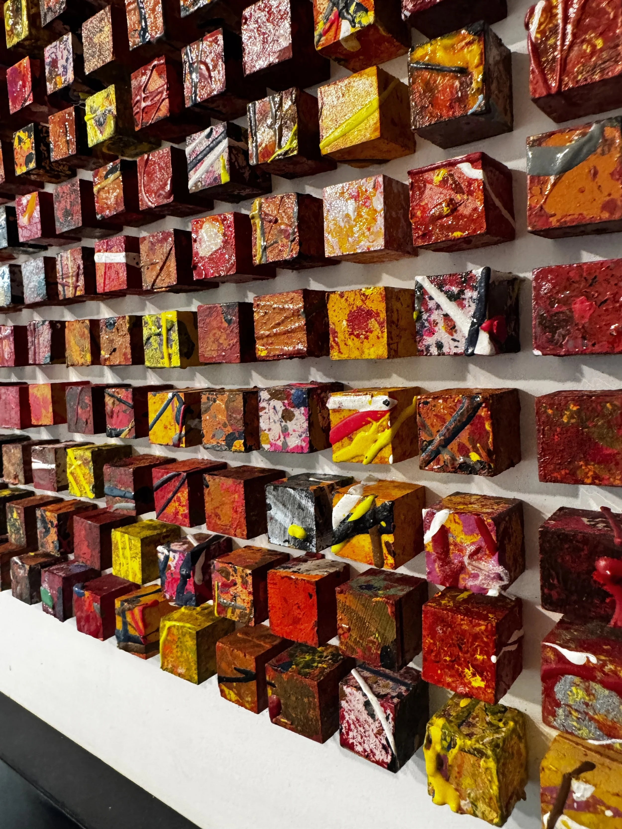 Multiple colorful, abstract painted cubes mounted on a wall in a grid pattern.