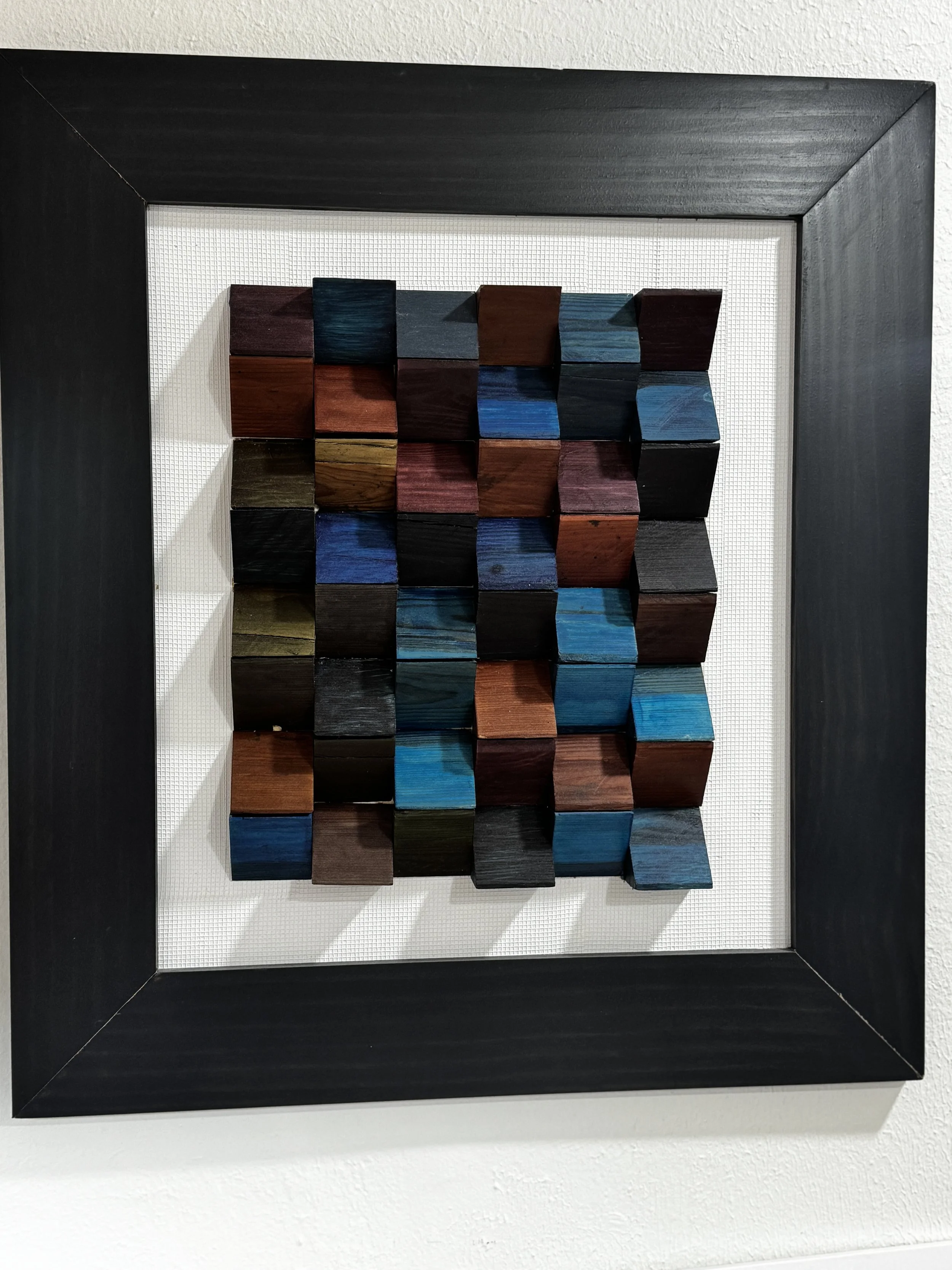 A framed 3D wall art piece featuring multicolored wooden cubes arranged in a grid pattern.