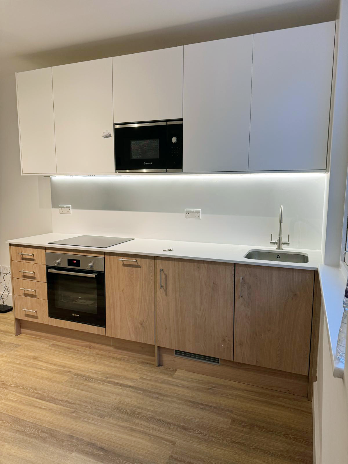 Modern kitchen with white cabinets, built-in microwave, stovetop, oven, and wooden lower cabinets. Includes a sink and hardwood flooring.