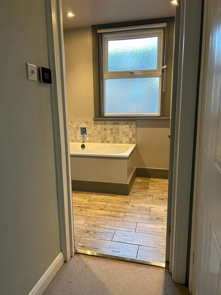 Modern bathroom with wood-like tile flooring, a bathtub, and frosted window.