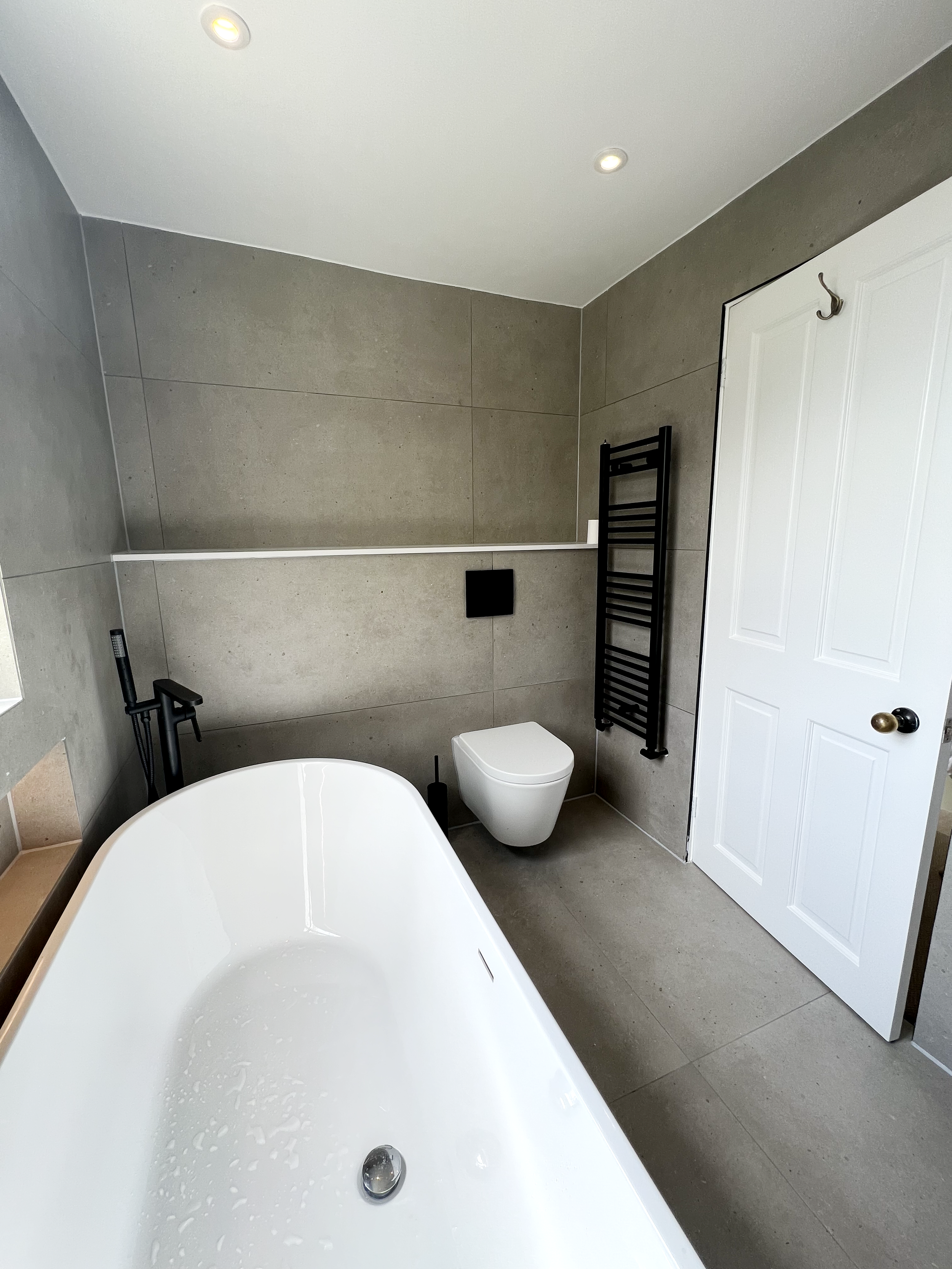 Modern bathroom with a freestanding bathtub, wall-mounted toilet, towel rack, and gray tiled walls.