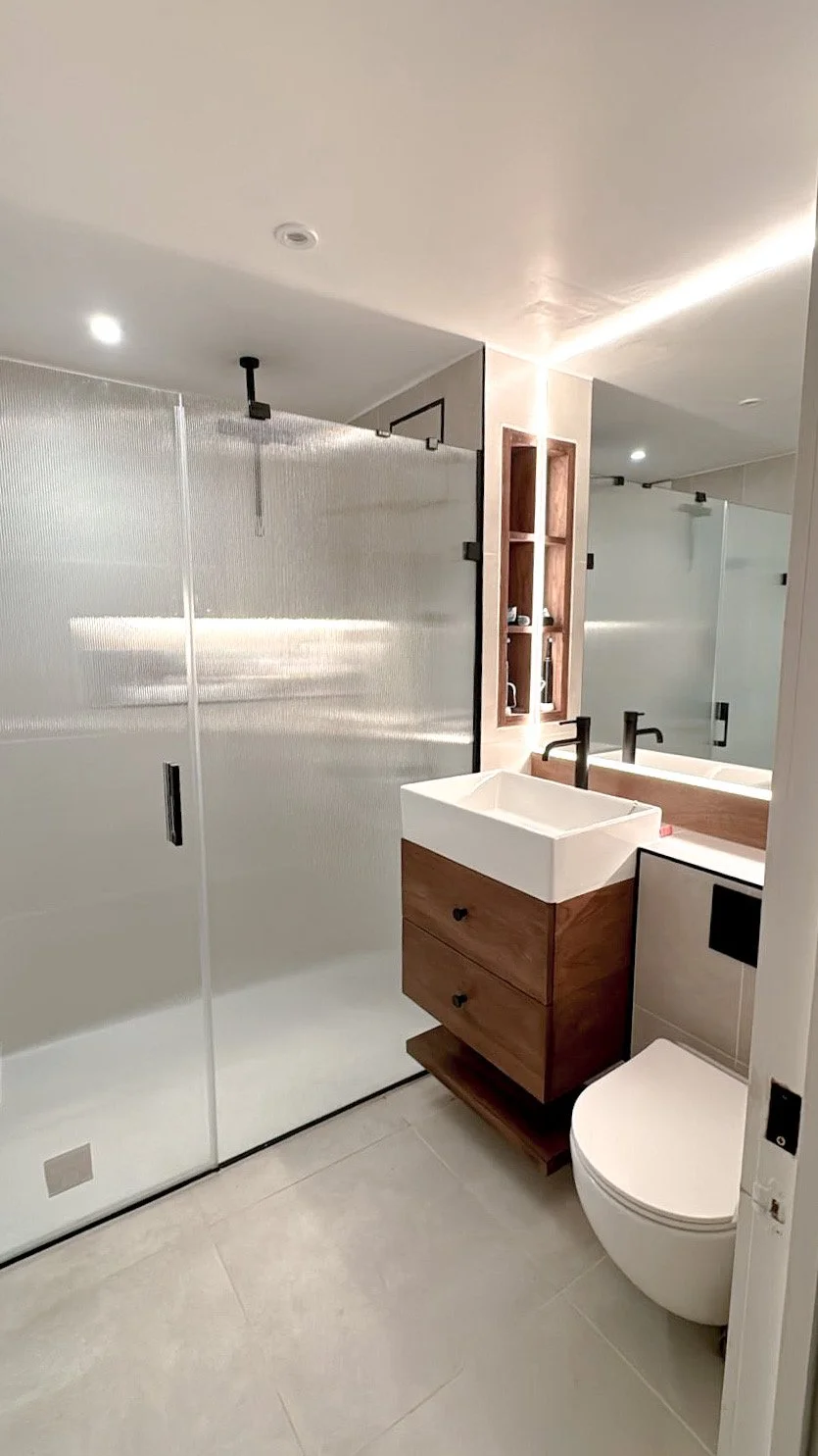 Modern bathroom with glass shower, white sink, and wooden cabinet.