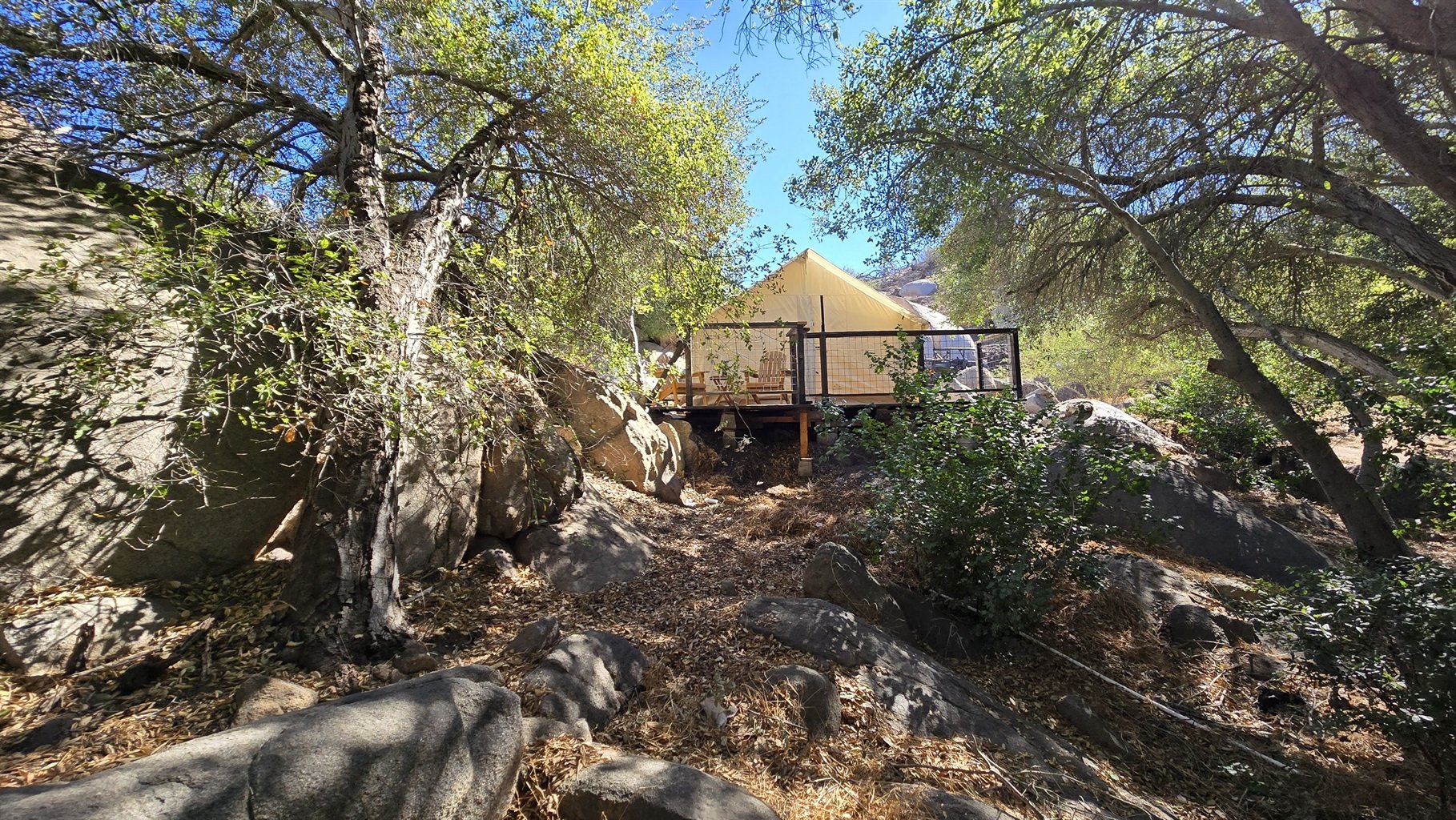 Canvas tent cabin on elevated platform surrounded by trees and rocks.