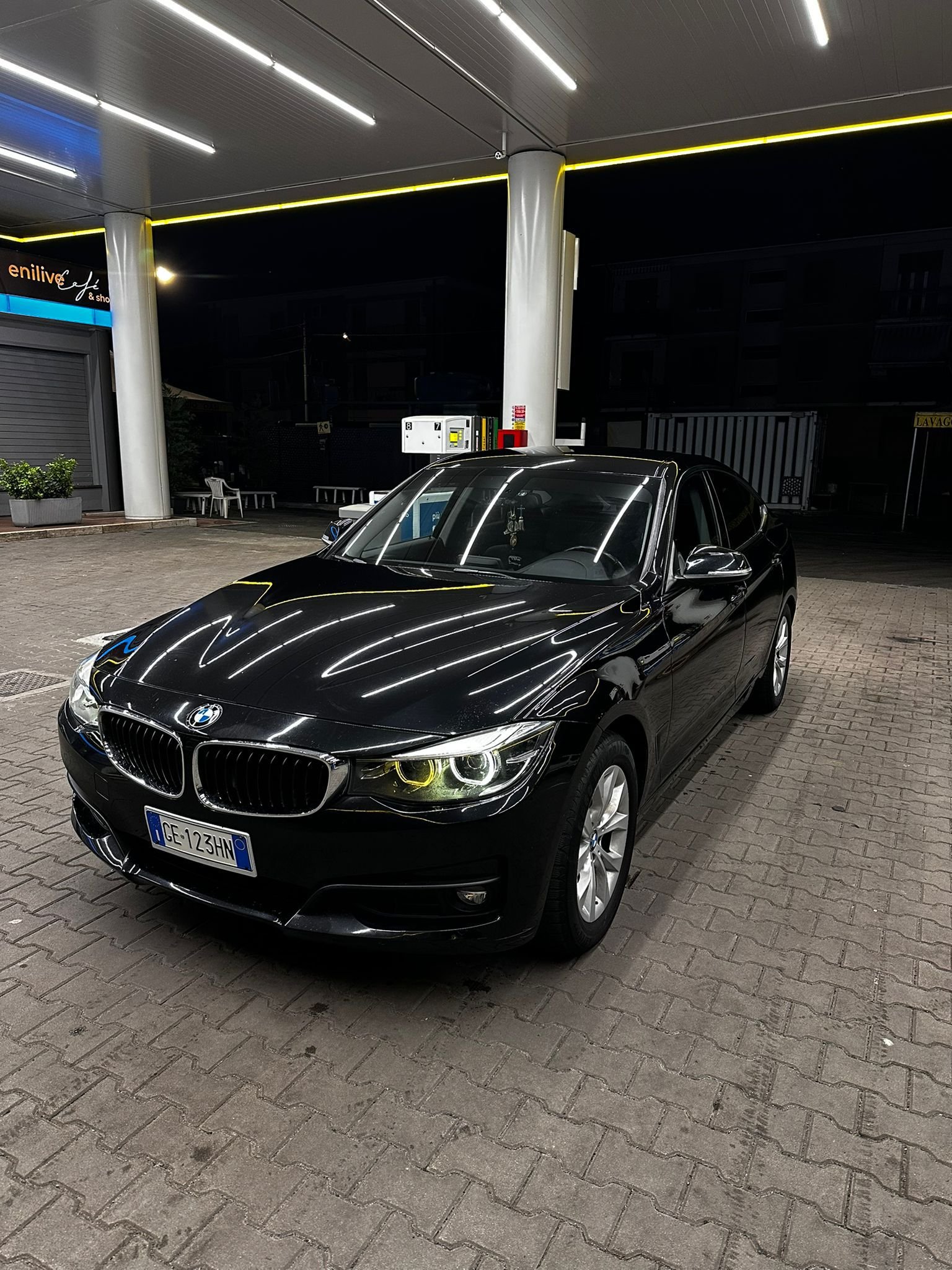 Auto BMW nero parcheggiata sotto una pensilina di una stazione di servizio di notte.
