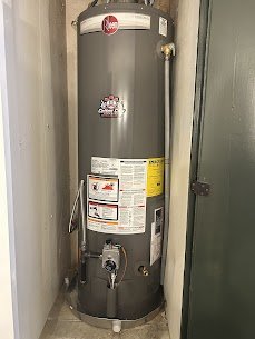 A tall, gray water heater with labels and controls, located in a utility closet next to a door.