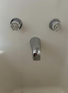 Two water supply valves above a faucet spout on a white wall.