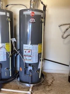 A black water heater tank installed in a basement, with pipes and electrical connections attached.