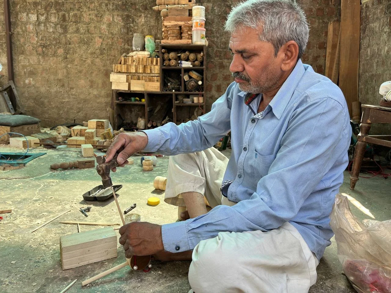 An older man with gray hair and a beard working on a woodworking project in a workshop, using a saw and a wooden piece.